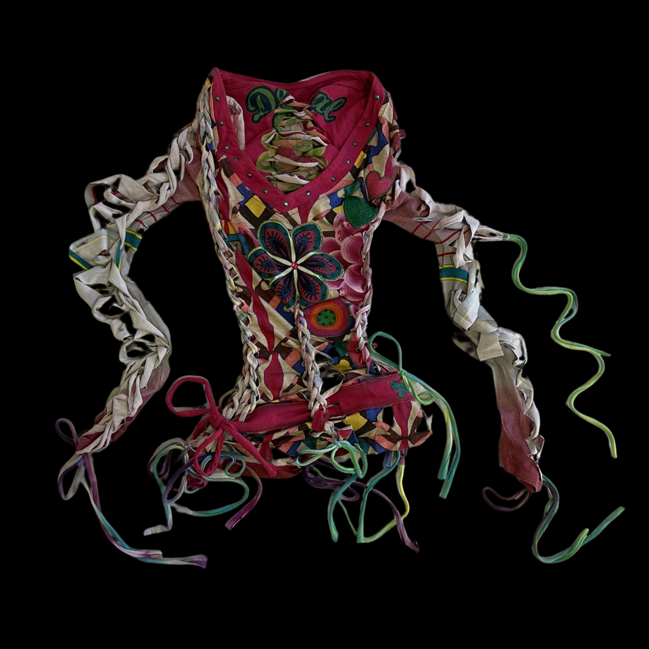 Colorful, intricately woven fabric sculpture resembling a dress, with laces, ribbons, and decorative patches, set against a black background.