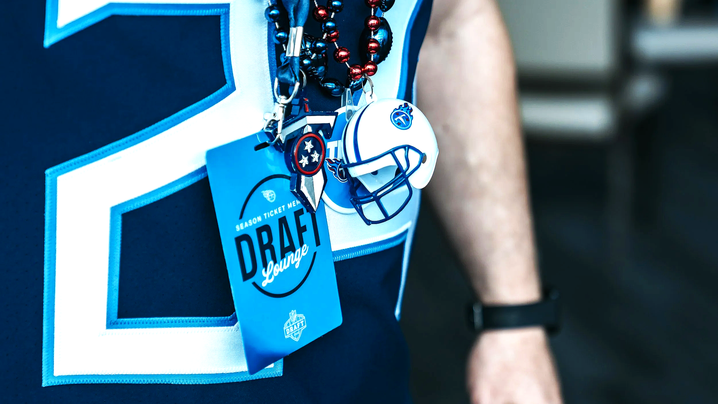 Close-up of a fan's Titans jersey with the number 59, a 'Draft Lounge' credential Andro Design Co. designed, and multiple beads, a whistle, keys, and a lanyard with Tennessee Titans logos hanging around the neck.