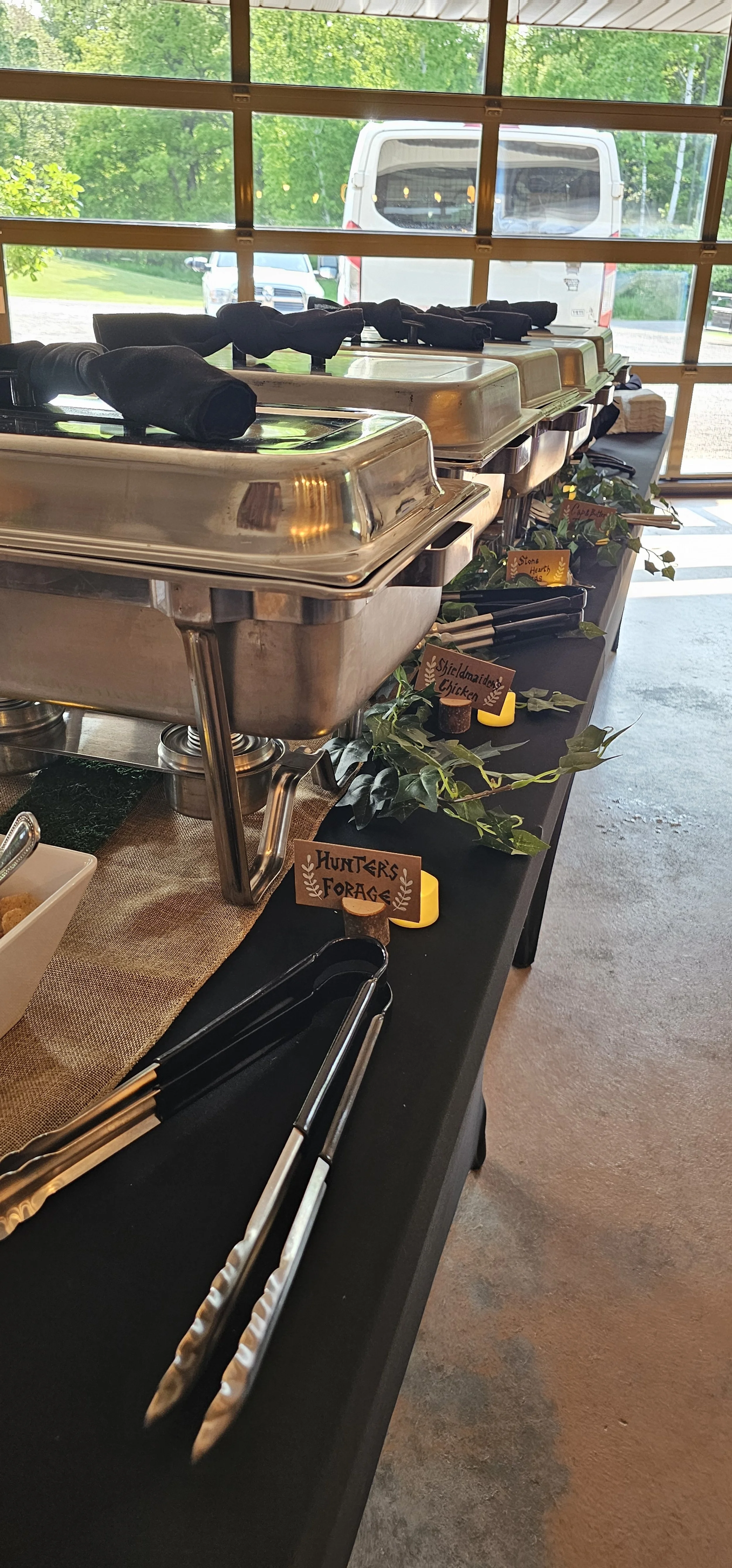 Viking & Enchanted Forest themed buffet setup featuring custom dish labels and rustic greenery décor. Each dish was given a unique name—like Hunter’s Forage and Shieldmaiden’s Chicken—to create an immersive dining experience blending Norse legend wit