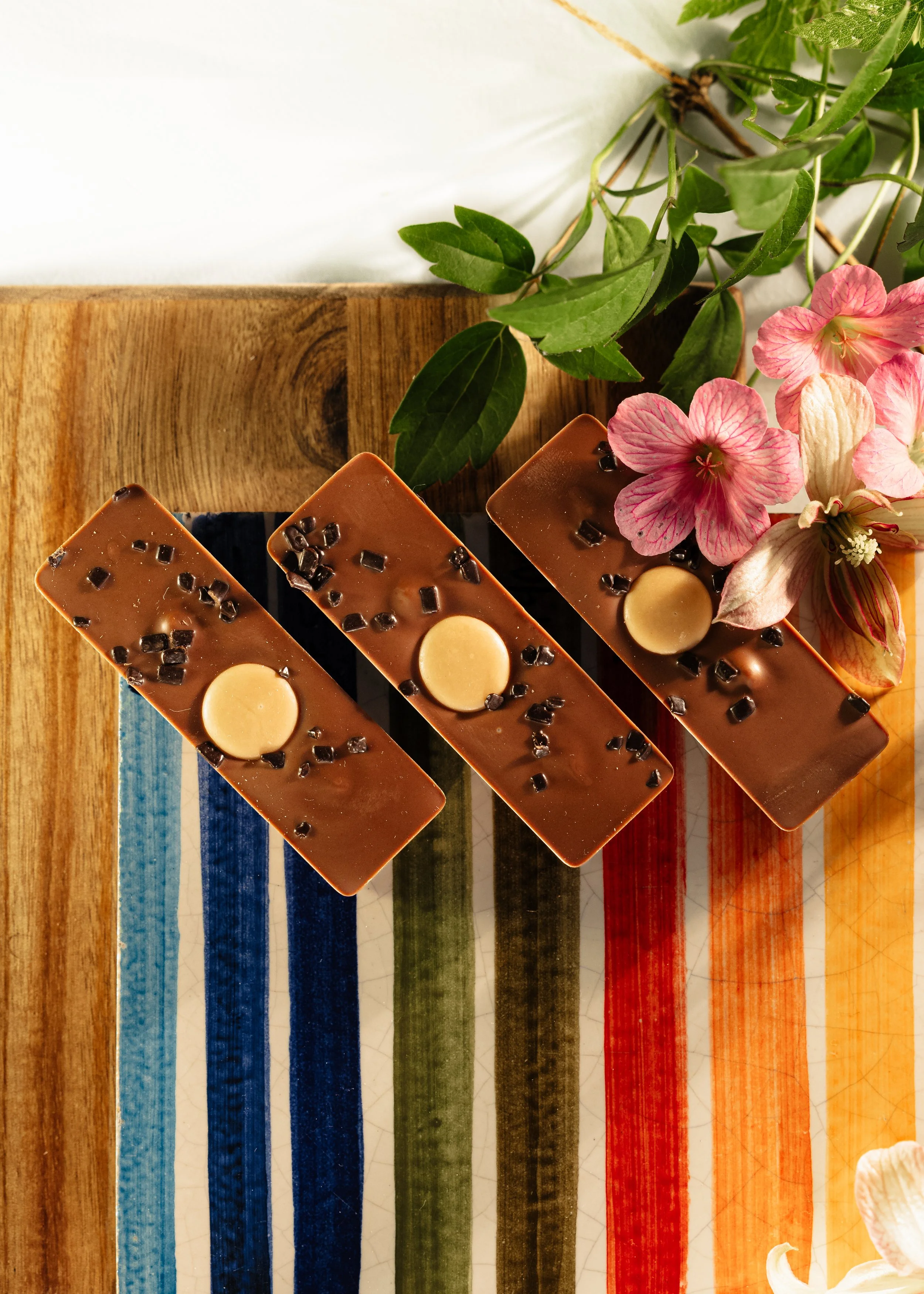 Chokolade med pynt af chokoladestykker og cirkelformet hvid chokolade, anrettet på fliser med farverige striber.