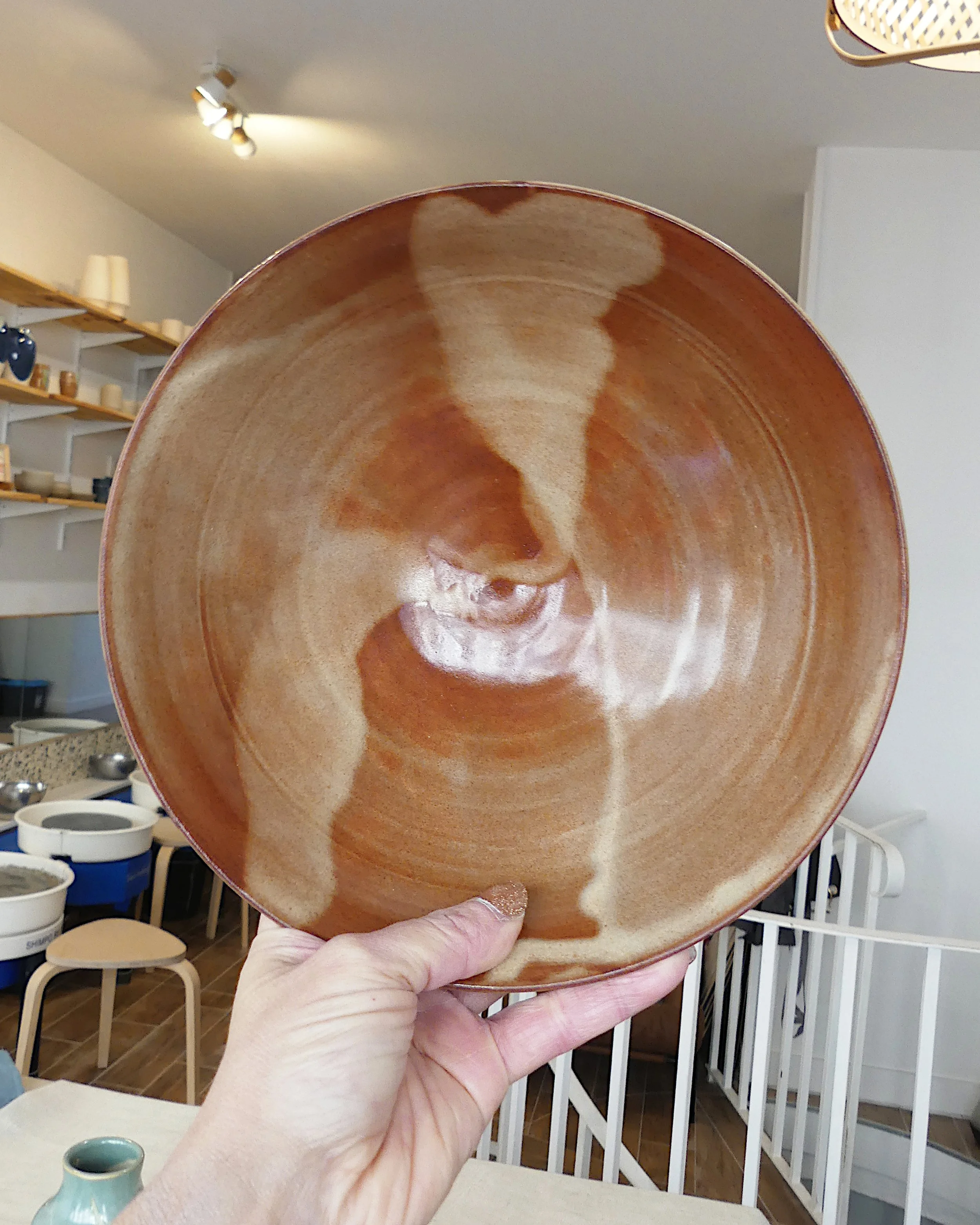 Un saladier ambrée tenu à bout de bras, derrière l'atelier de céramique est visible