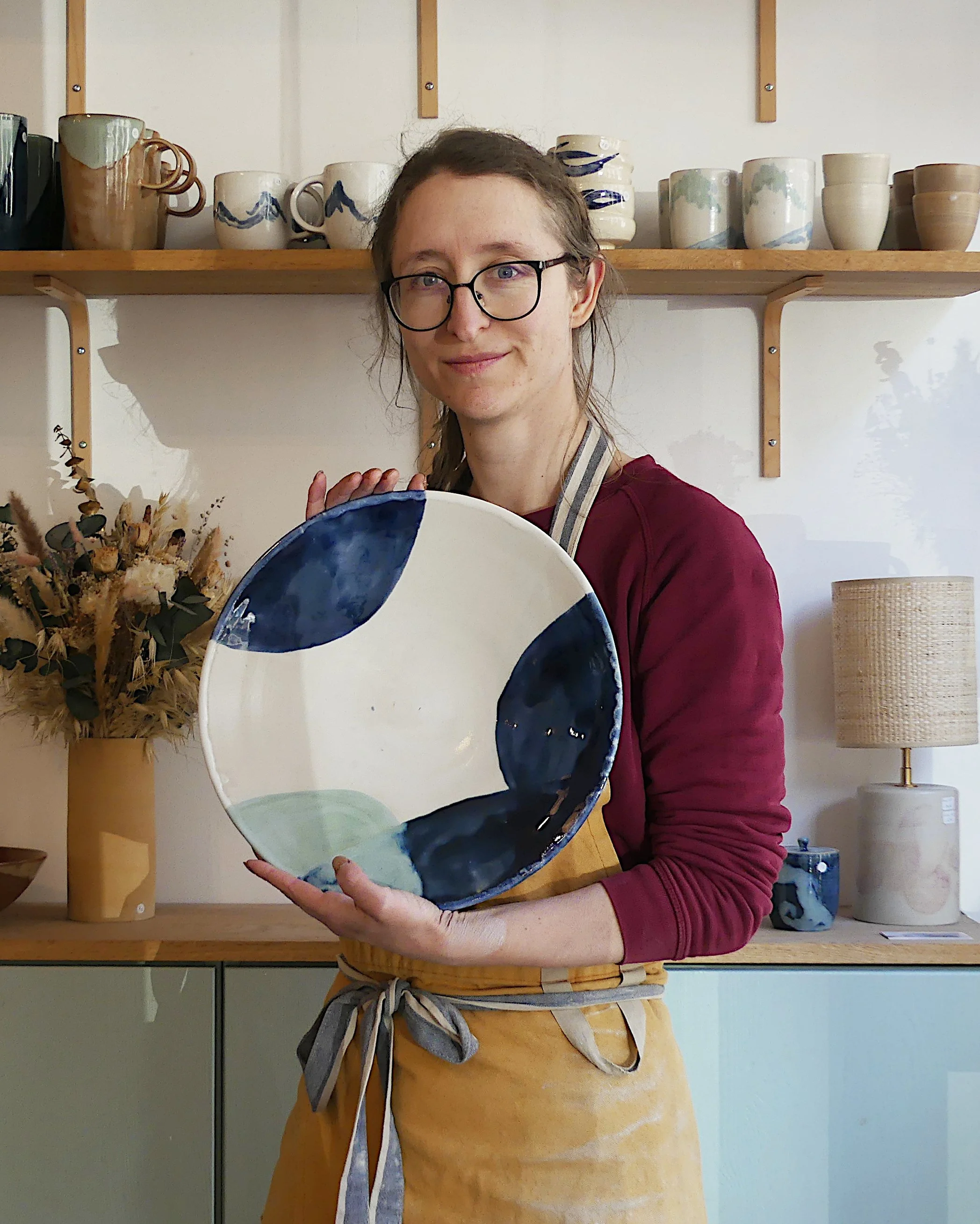 Marion, artisane céramiste, pose avec un plat blanc bleu et vert entre les mains