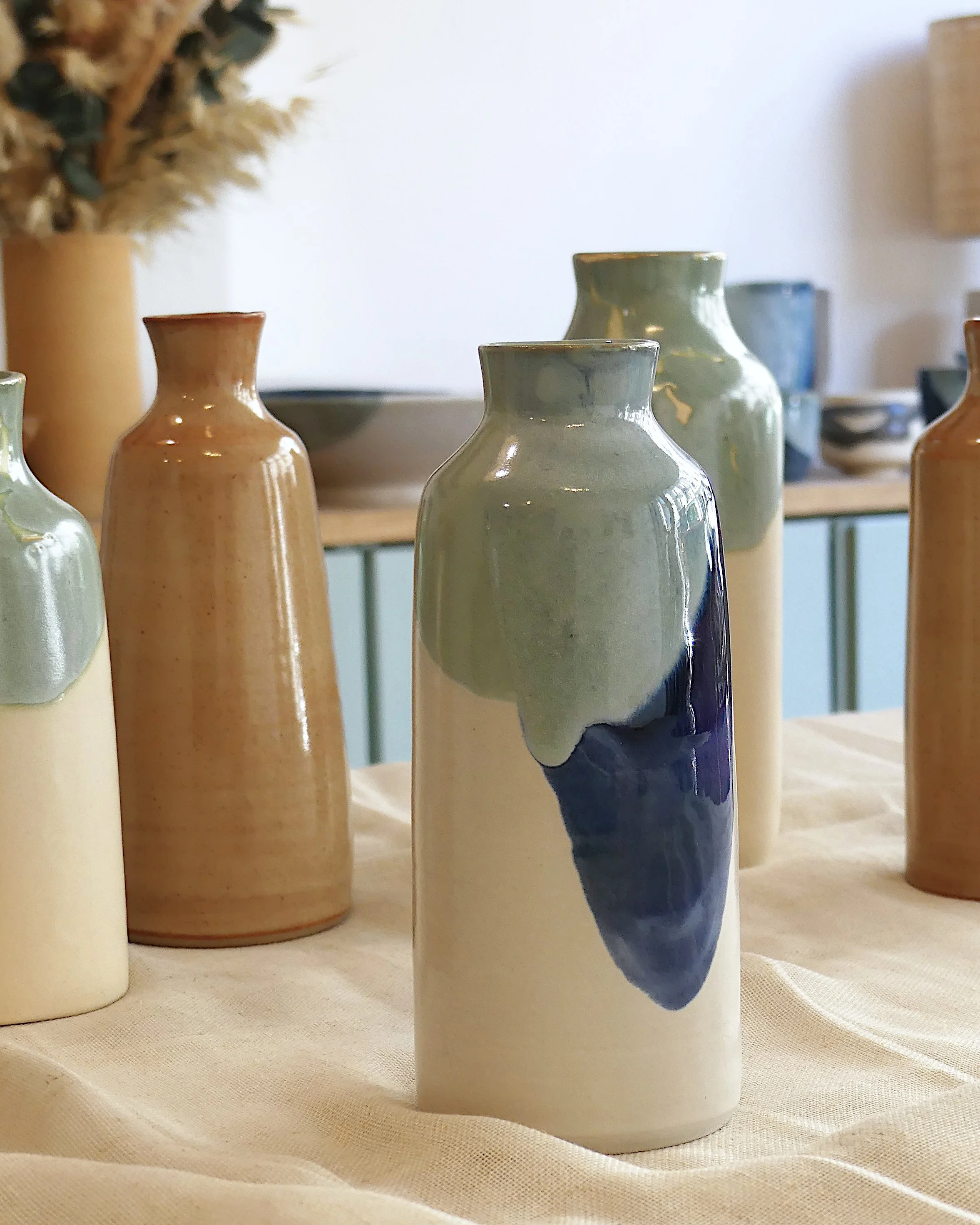 Au premier plan un bouteille en céramique de couleur blanche, bleue et verte, derrière d'autres bouteilles.