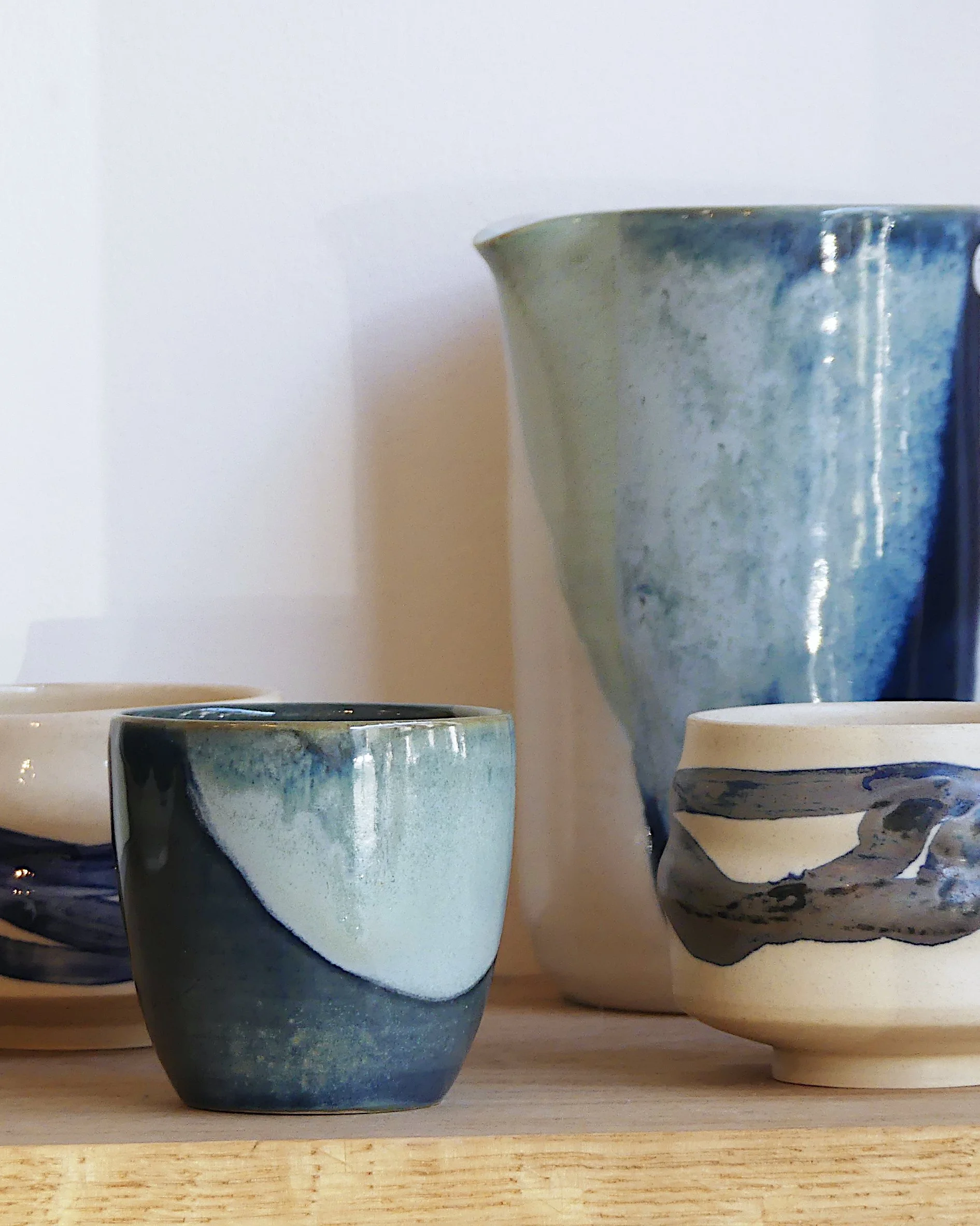 Une tasse bleu et verte au premier plan, derrière un pichet dans les même tonalités de couleurs