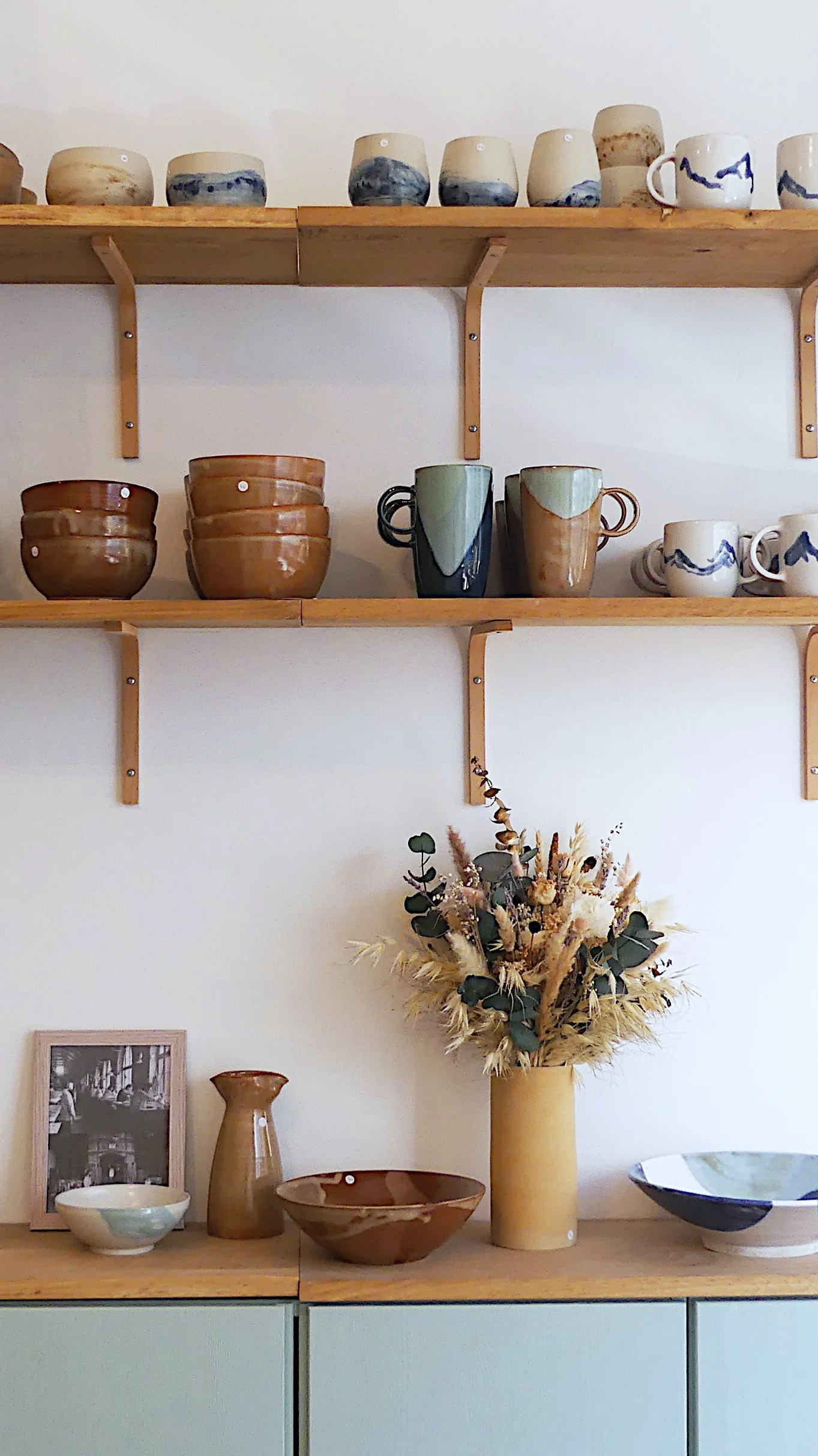 les étagères de la boutique remplis de pièces en céramiques de couleurs blanches, bleues, vertes et ambrées 