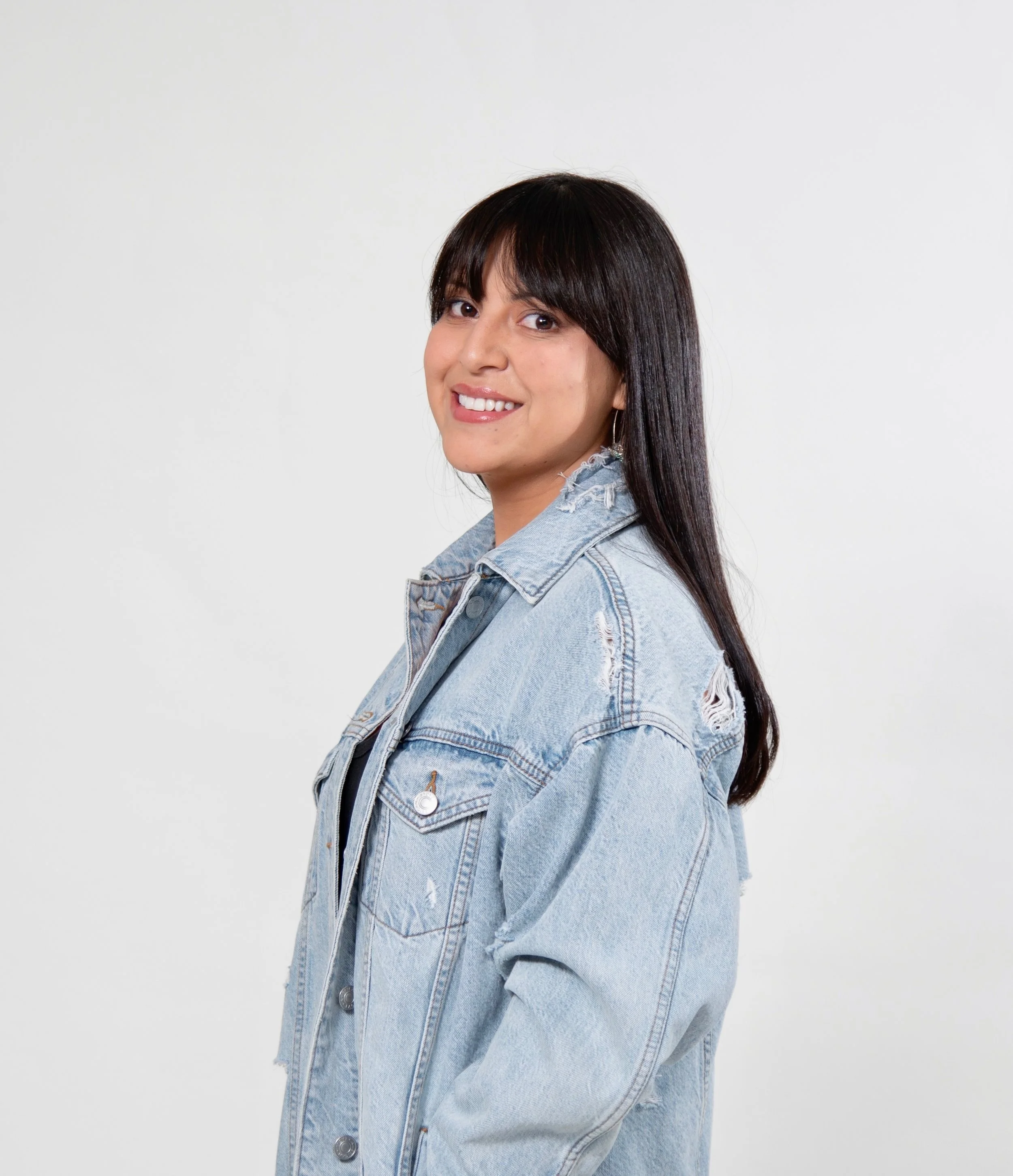 Woman wearing a denim jacket with long dark hair smiling