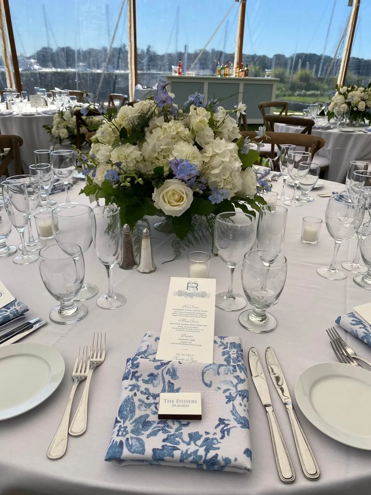 Close up of a table arrangement with blues and whites set under a wedding tent.jpeg