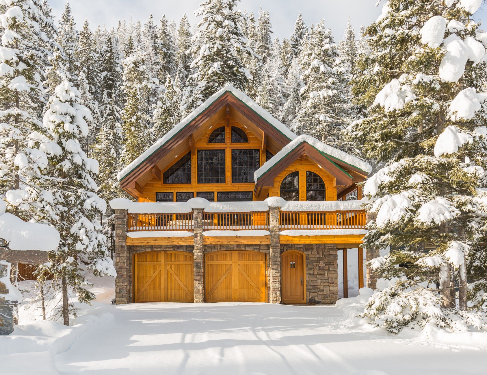 Snow-covered house with wooden accents and large windows, surrounded by snow-laden trees in winter.