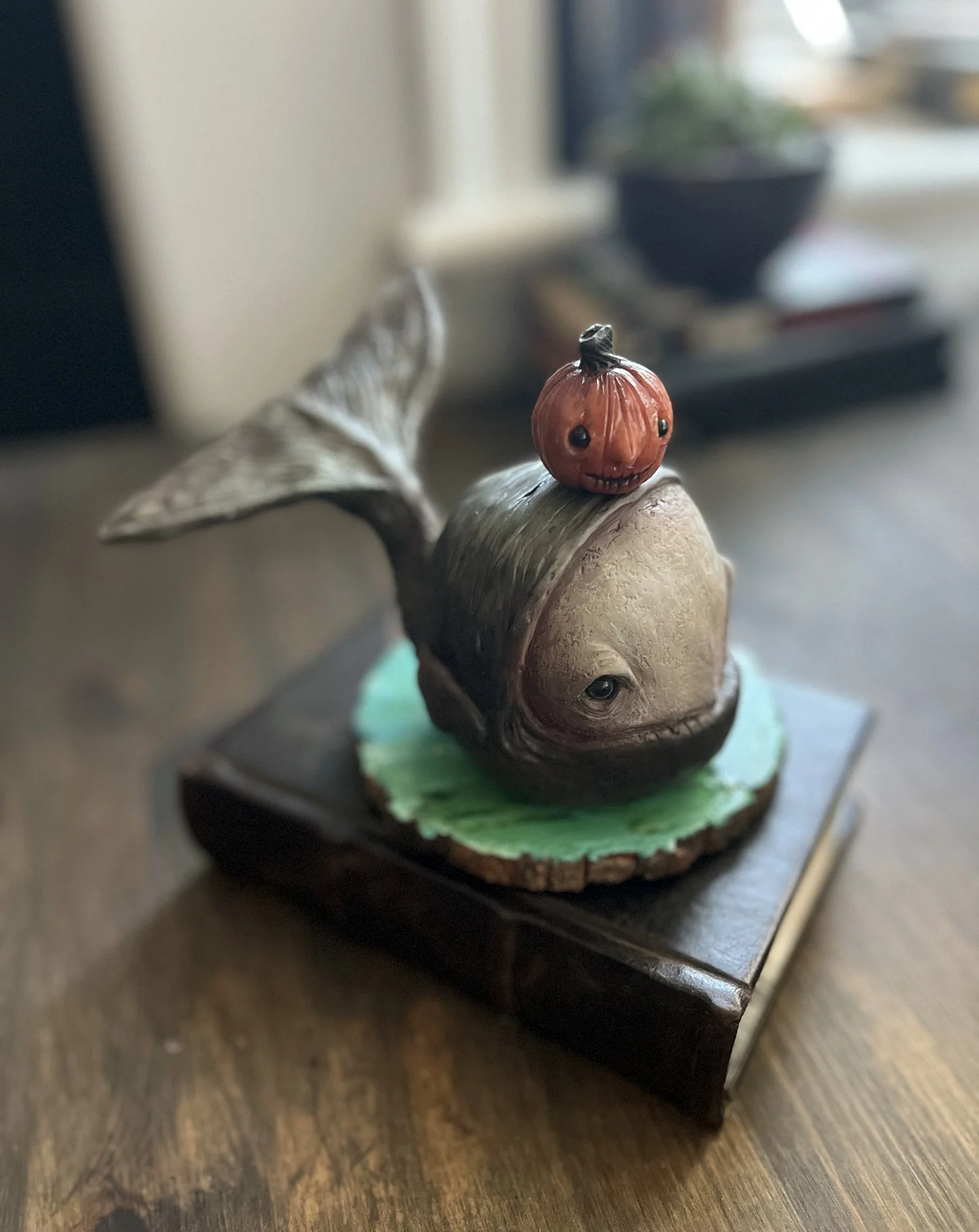 A small decorative sculpture of a snail with a pumpkin on its back, featuring a carved face, positioned on a wooden surface.