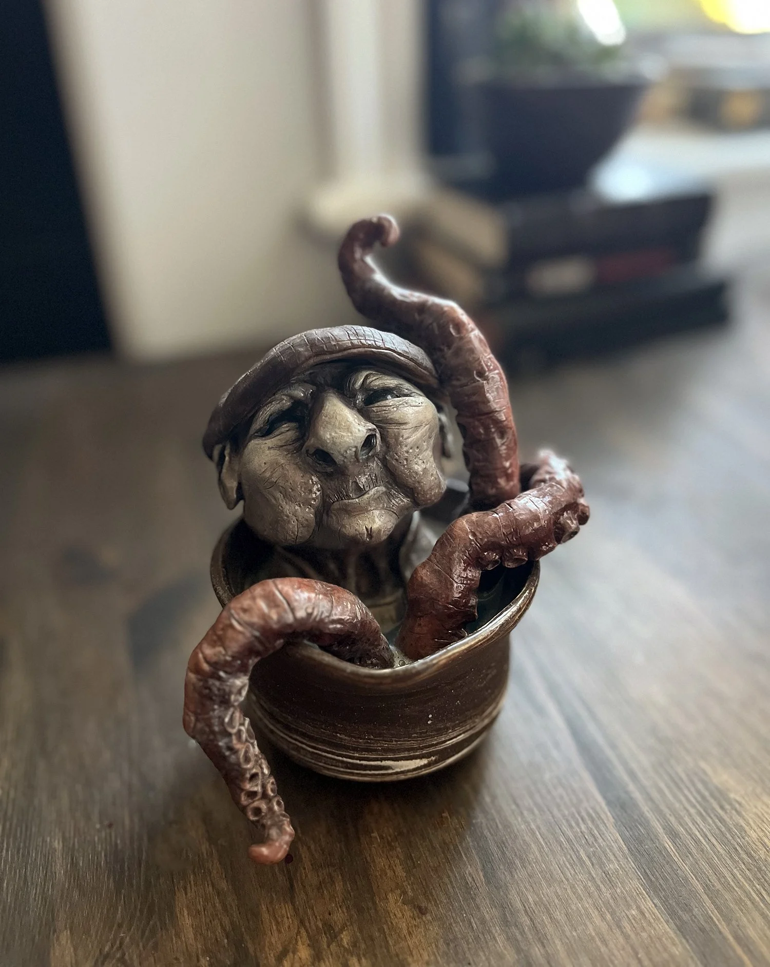 A decorative sculpture of a man's face with one eye open and a serious expression, holding a red octopus in a small brown ceramic pot.