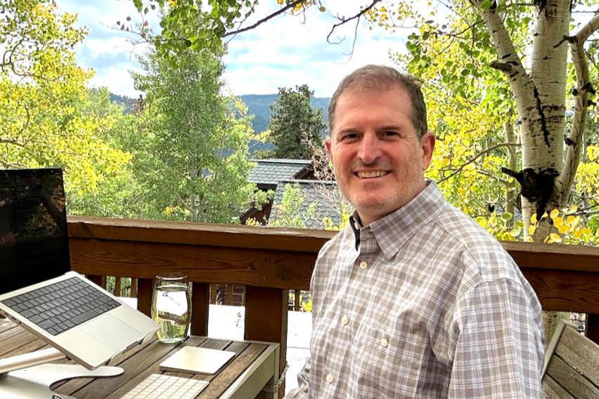 Stan Ajemian, IFS-informed coach at Being the Change Coaching, working at his table on a deck surrounded by golden aspen trees in Nederland, Colorado.