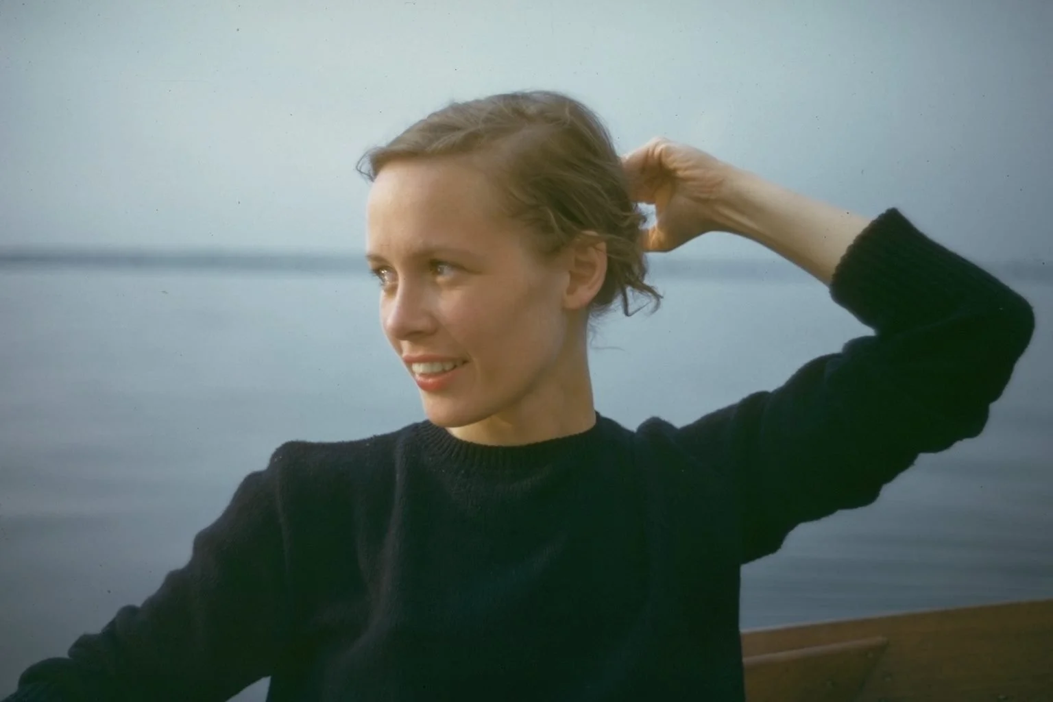 Sarah Waters mother Shurlee, with short, wavy blonde hair and fair skin smiling, wearing a black sweater, near a body of water during daytime.
