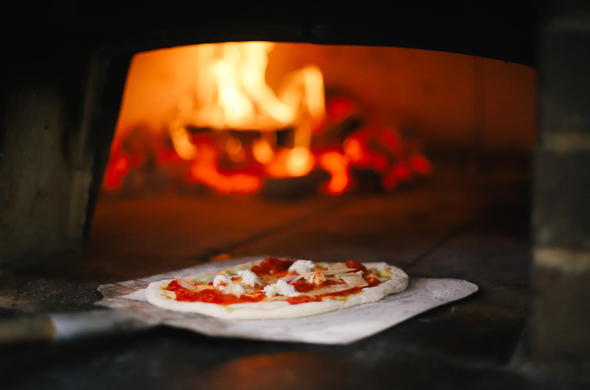 Pizza being baked in a pizza oven with flames visible inside.
