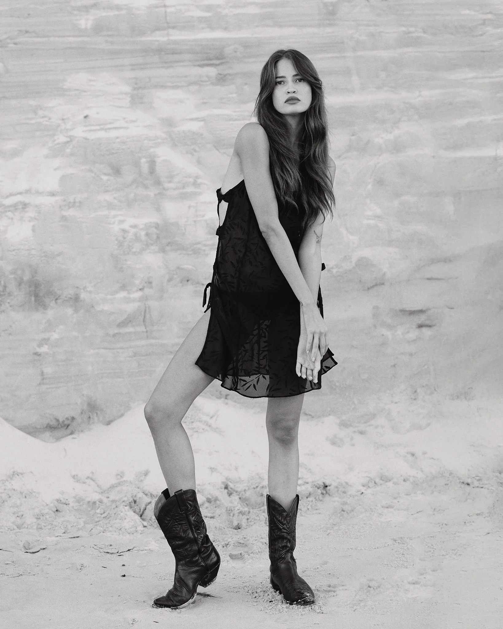 Editorial fashion portrait of a woman in a black dress and cowboy boots.