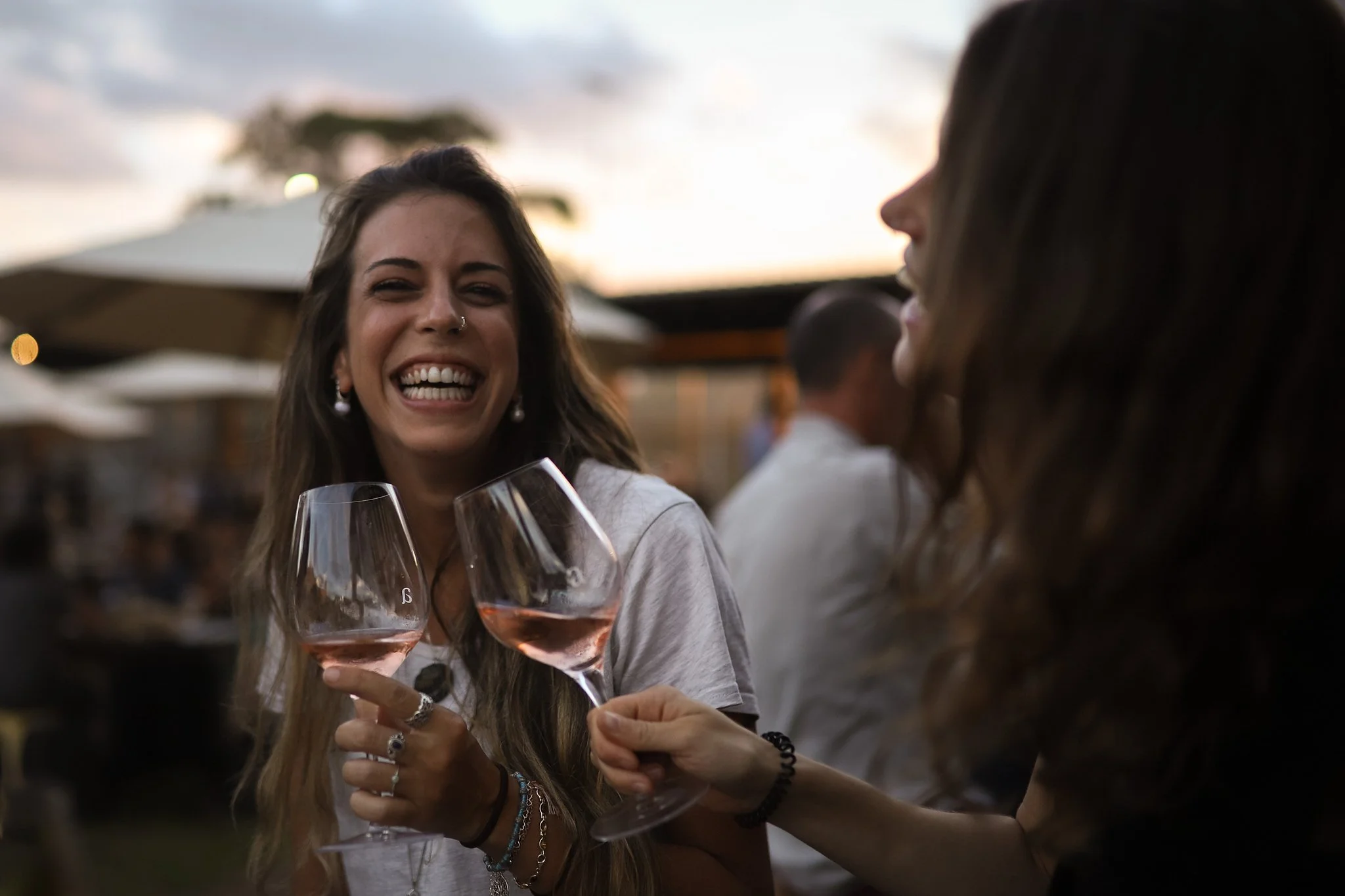 Two women smiling and clinking glasses of rosé wine outdoors during sunset.