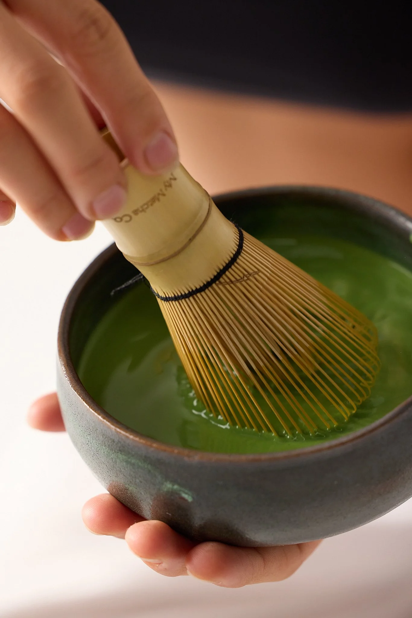 Close-up of hands whisking matcha in ceramic bowl with bamboo whisk – Byron Bay product photography