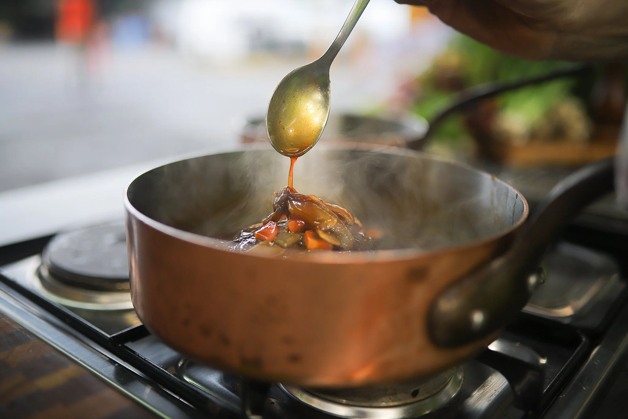 A ladle pouring gravy over cooked vegetables in a copper pot on a stove.