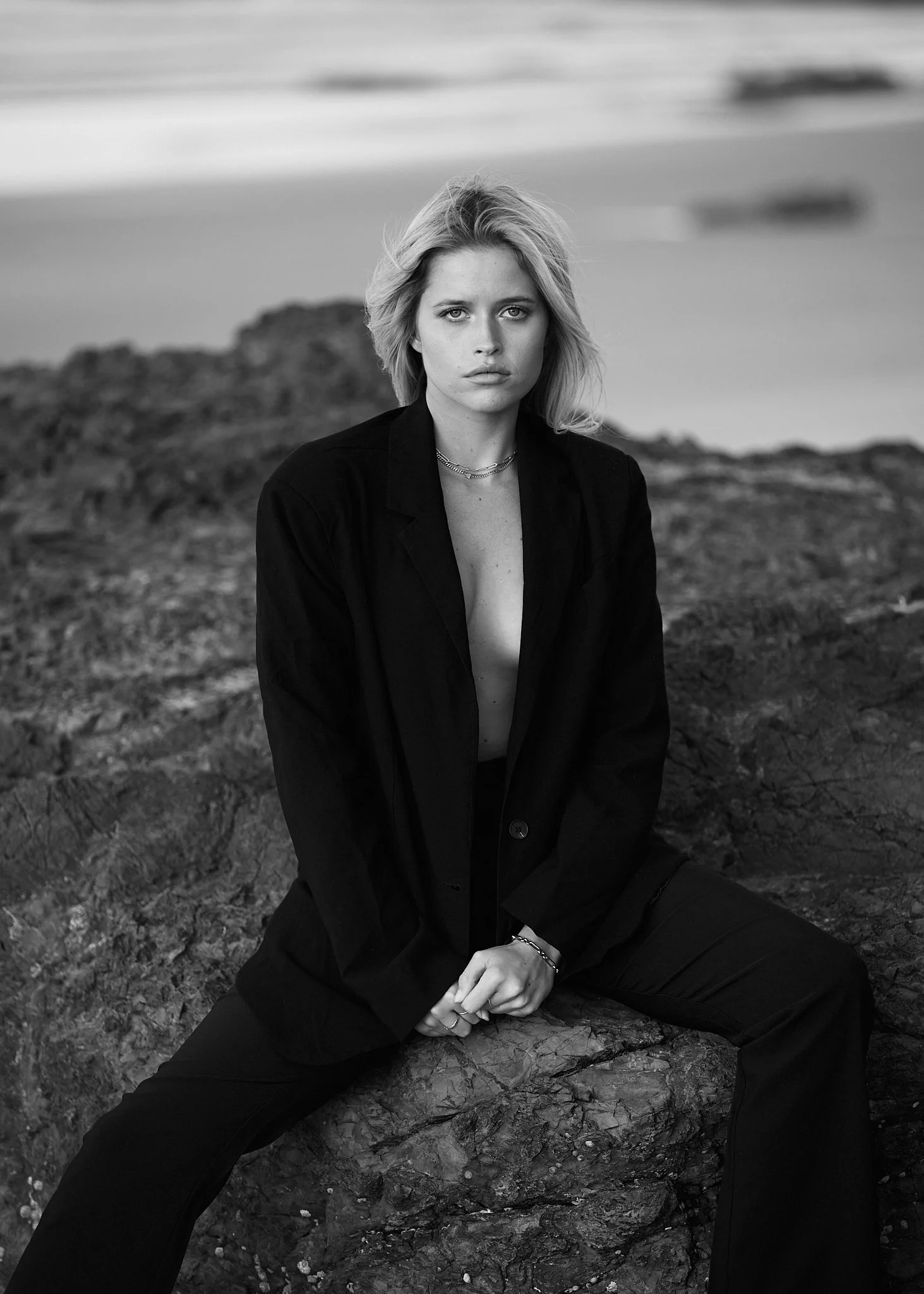 Fashion portrait of a woman on coastal rocks wearing a tailored jacket.