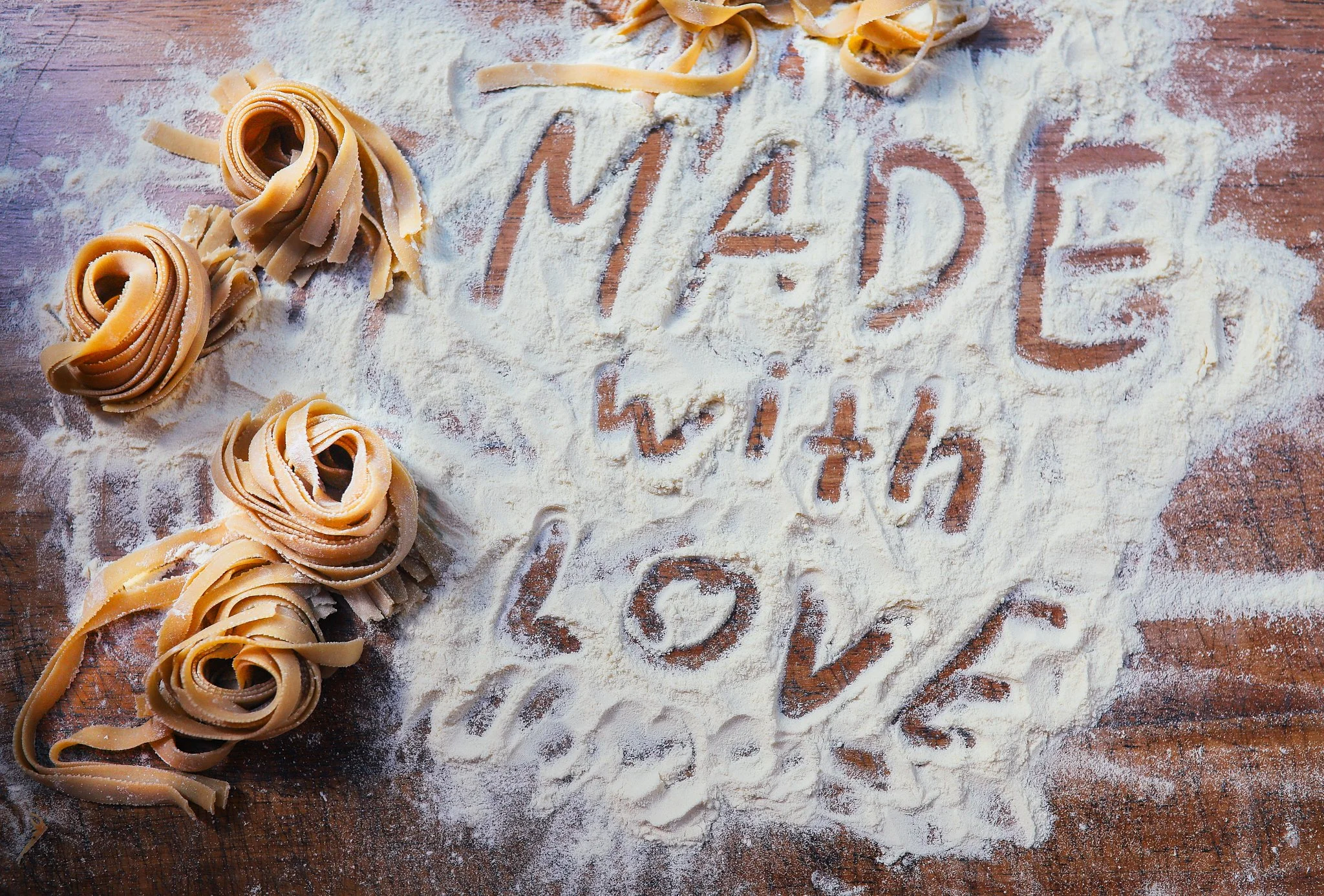 Uncovered pasta on a floured wooden surface with the words 'I love pasta' written in the flour.