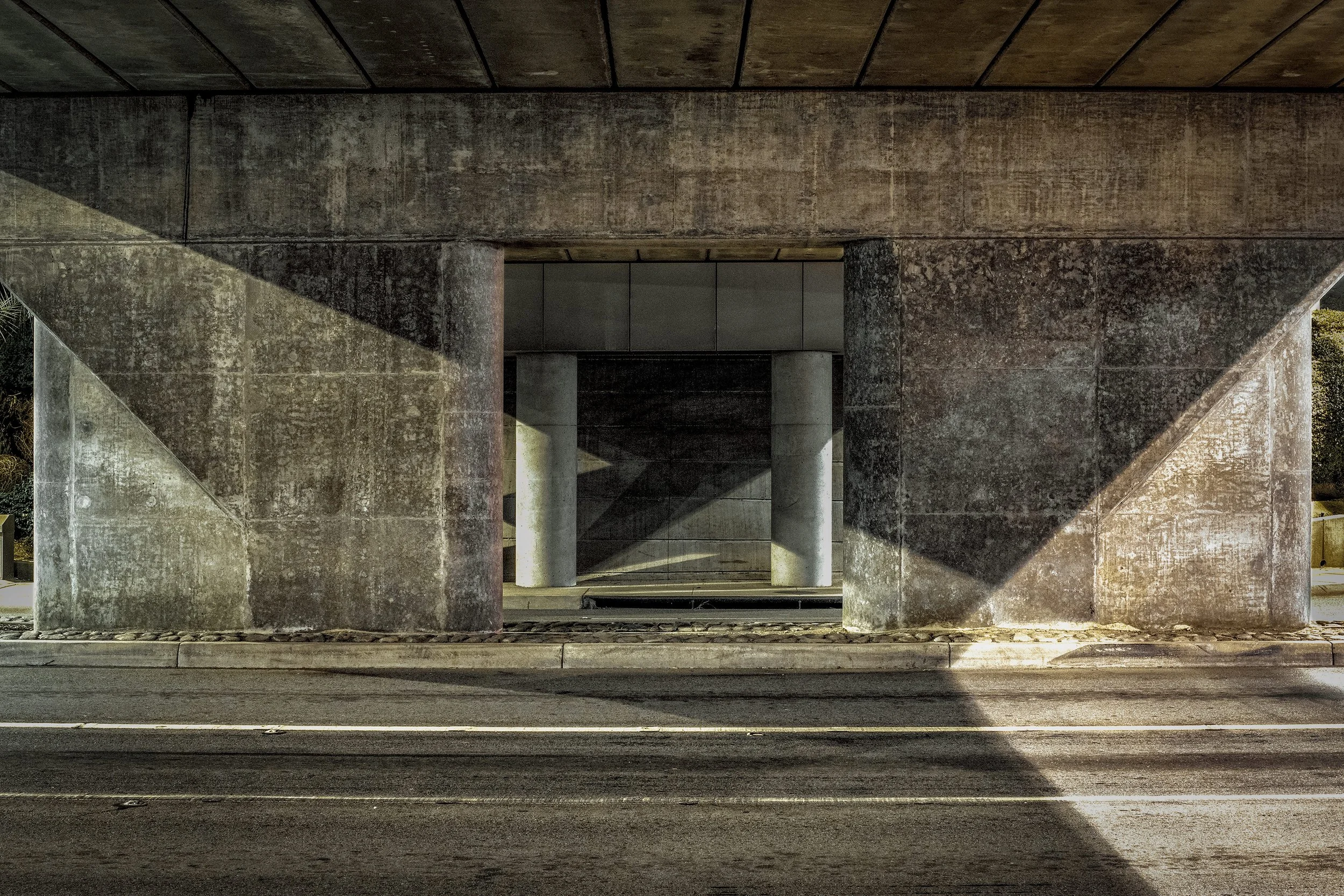 View of a concrete bridge structure with multiple supports and shadows cast on the ground.