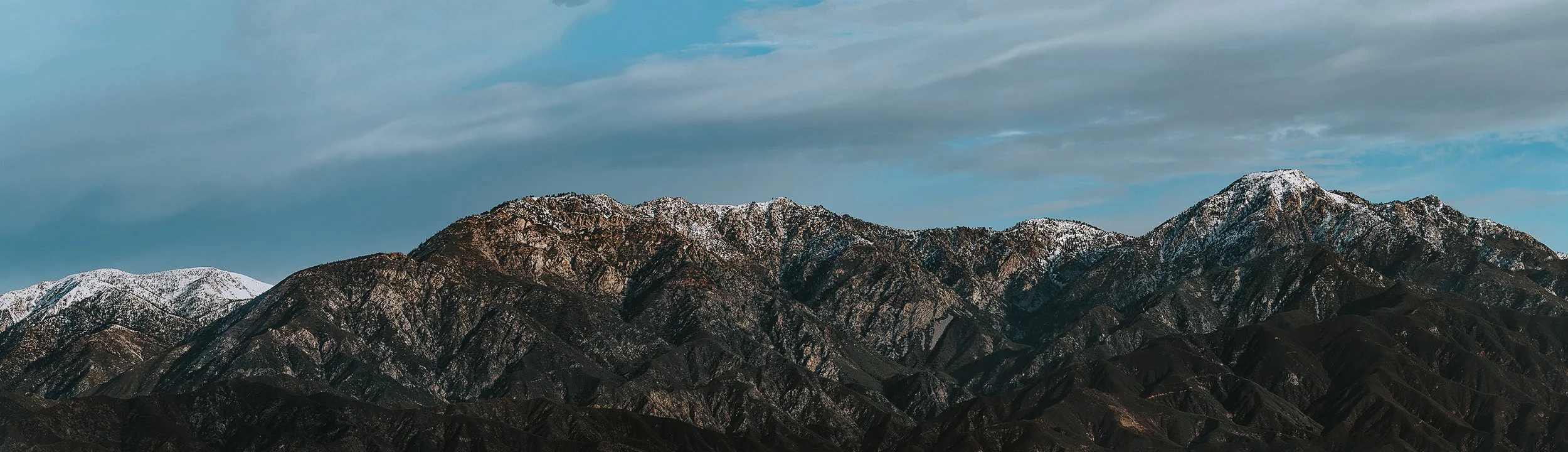 Snow-capped mountain range under a cloudy sky.
