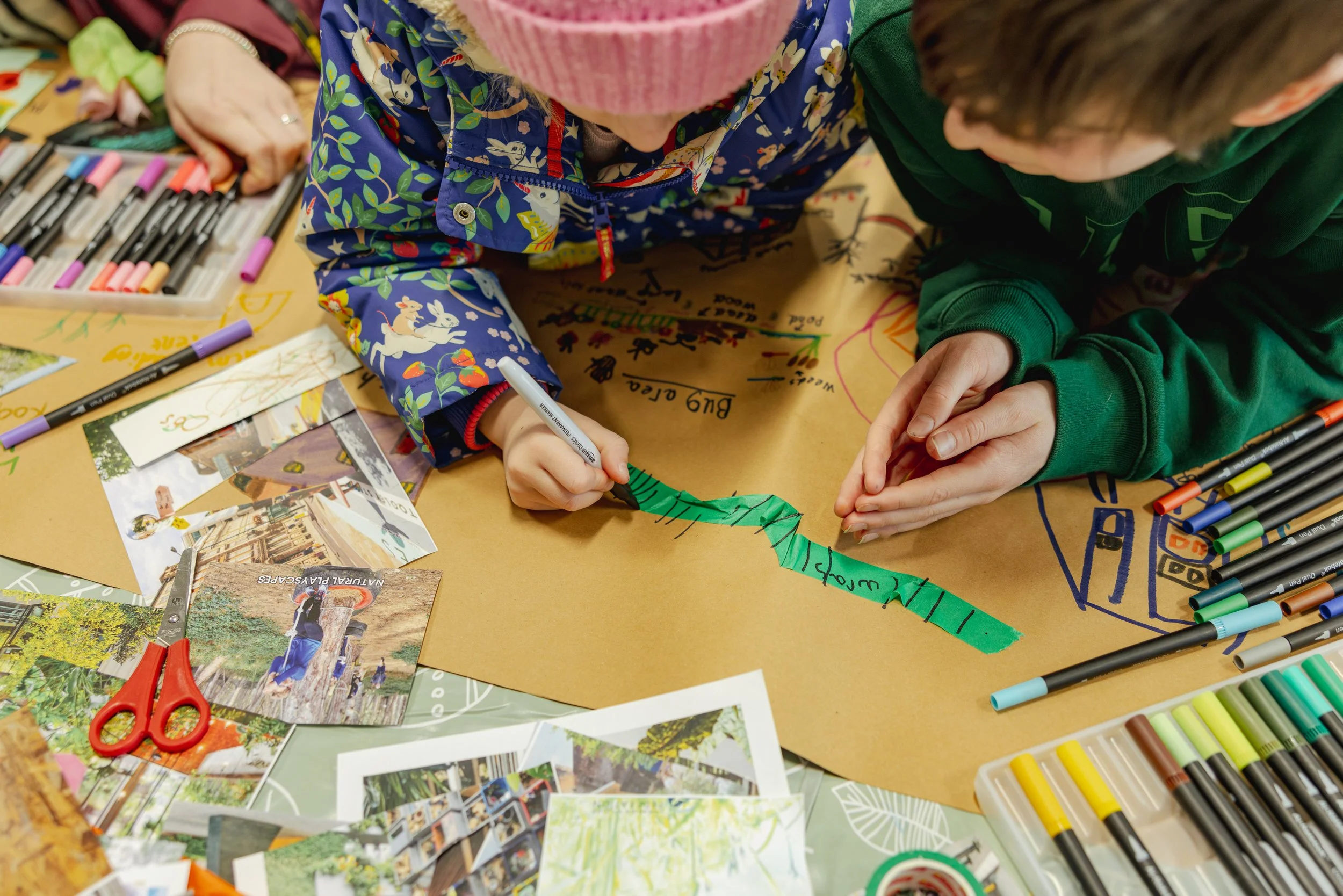 Close-up documentary workshop photography of children collaborating on a hands-on creative activity, drawing and crafting together during an educational workshop session.