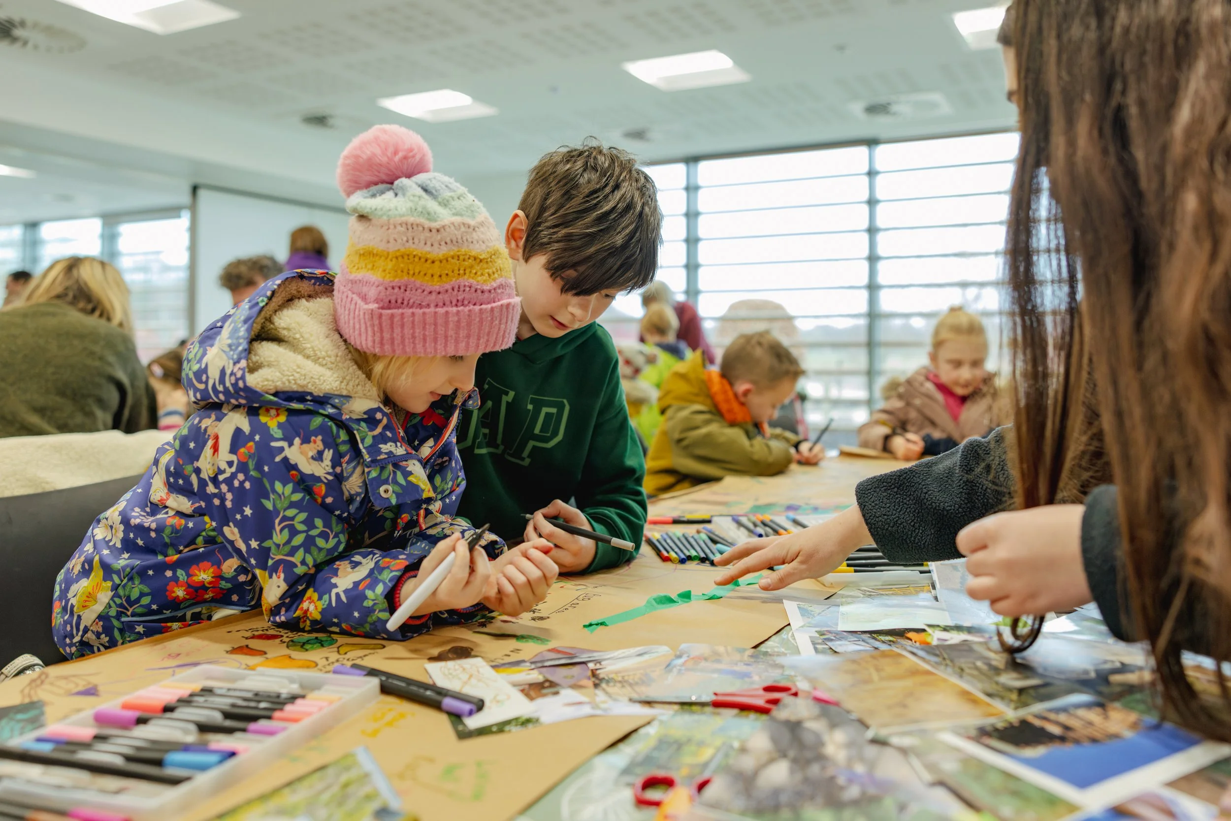 Candid documentary-style workshop photography capturing children collaborating on a creative group activity in a light-filled workshop setting.