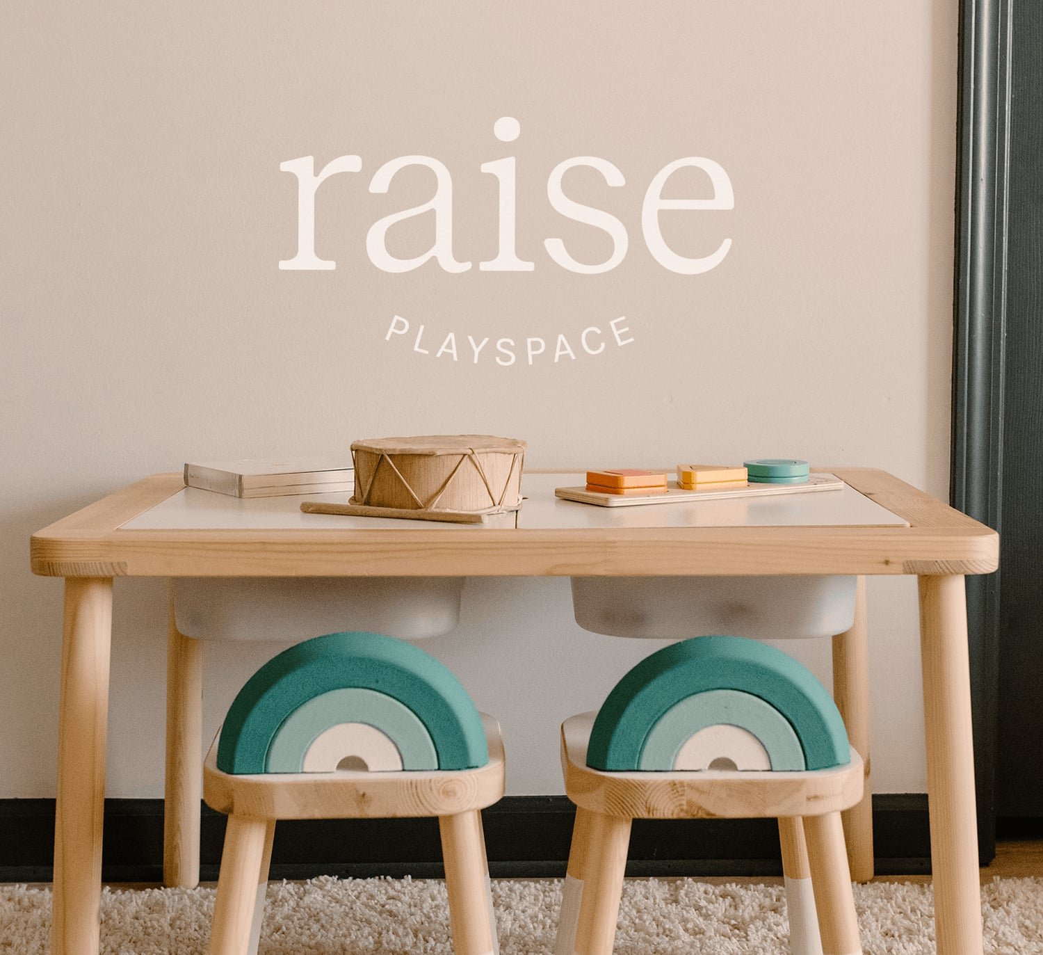 Minimalist kids’ playroom branding and Squarespace website design for Raise Playspace featuring custom logo design, natural wood furniture, and modern rainbow stools, designed to reflect a calm, inclusive, and family-centered environment.