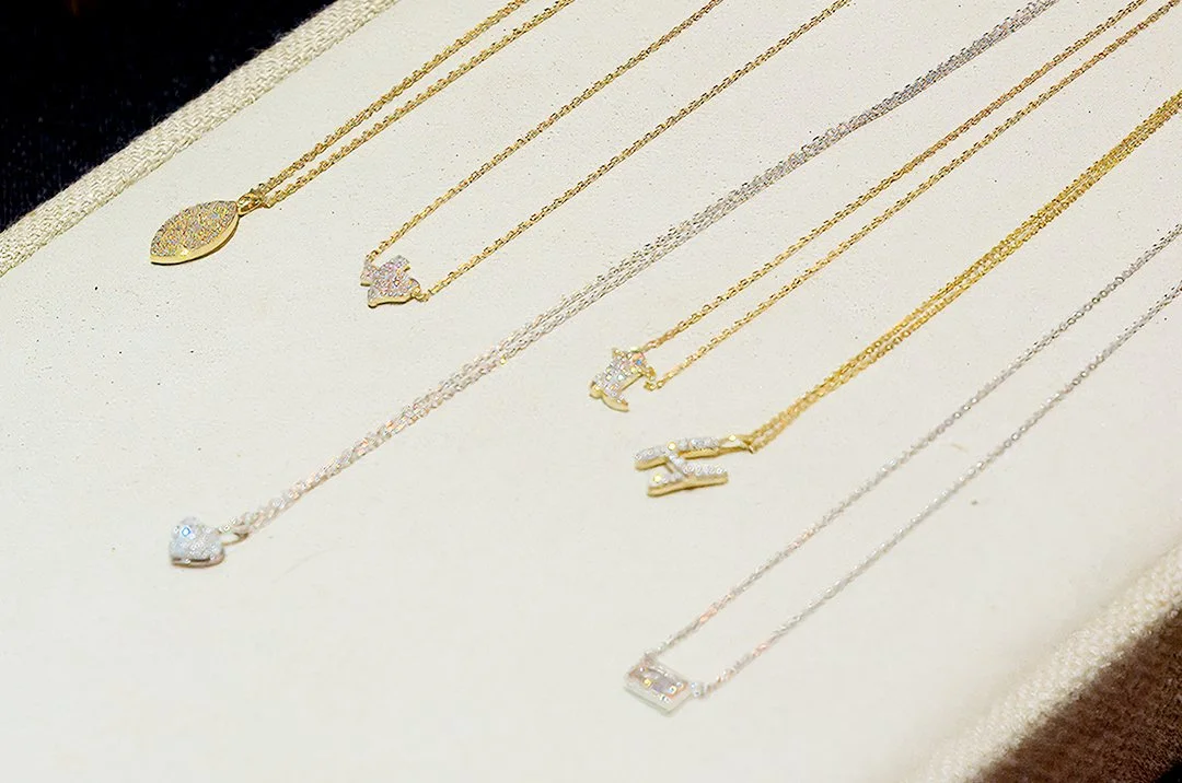 Collection of gold chain necklaces with various diamond-studded pendants on display. The pendants include shapes like ovals, hearts, and letters.