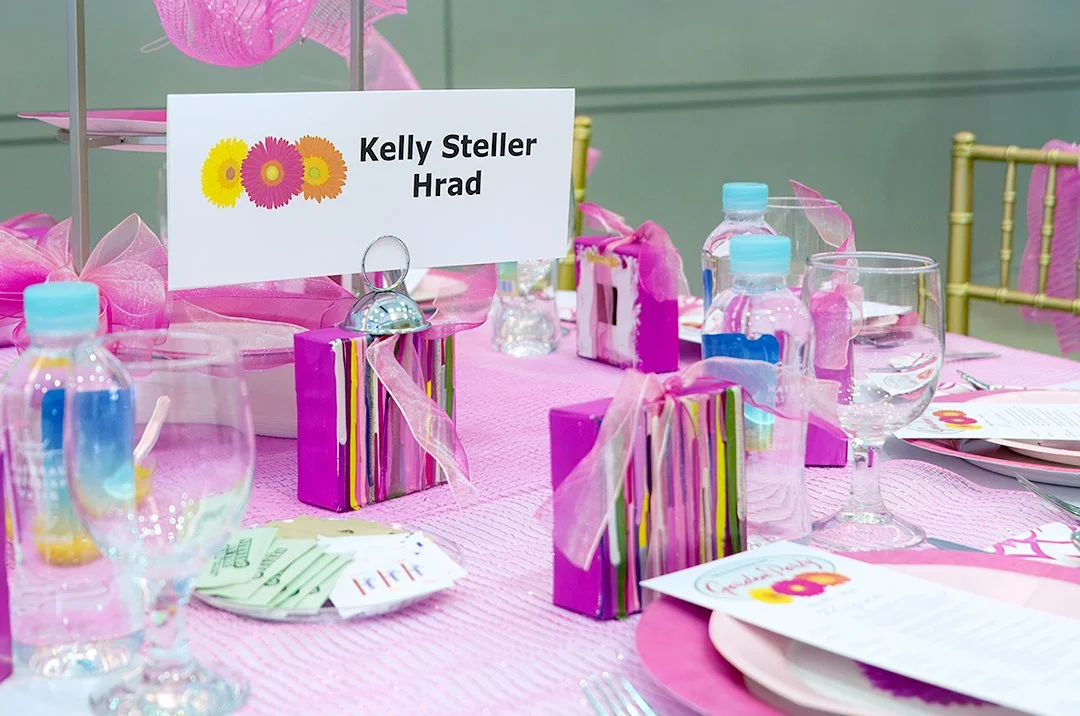 Pink-themed table setting with name card, decorated boxes, water bottles, glasses, and menus.