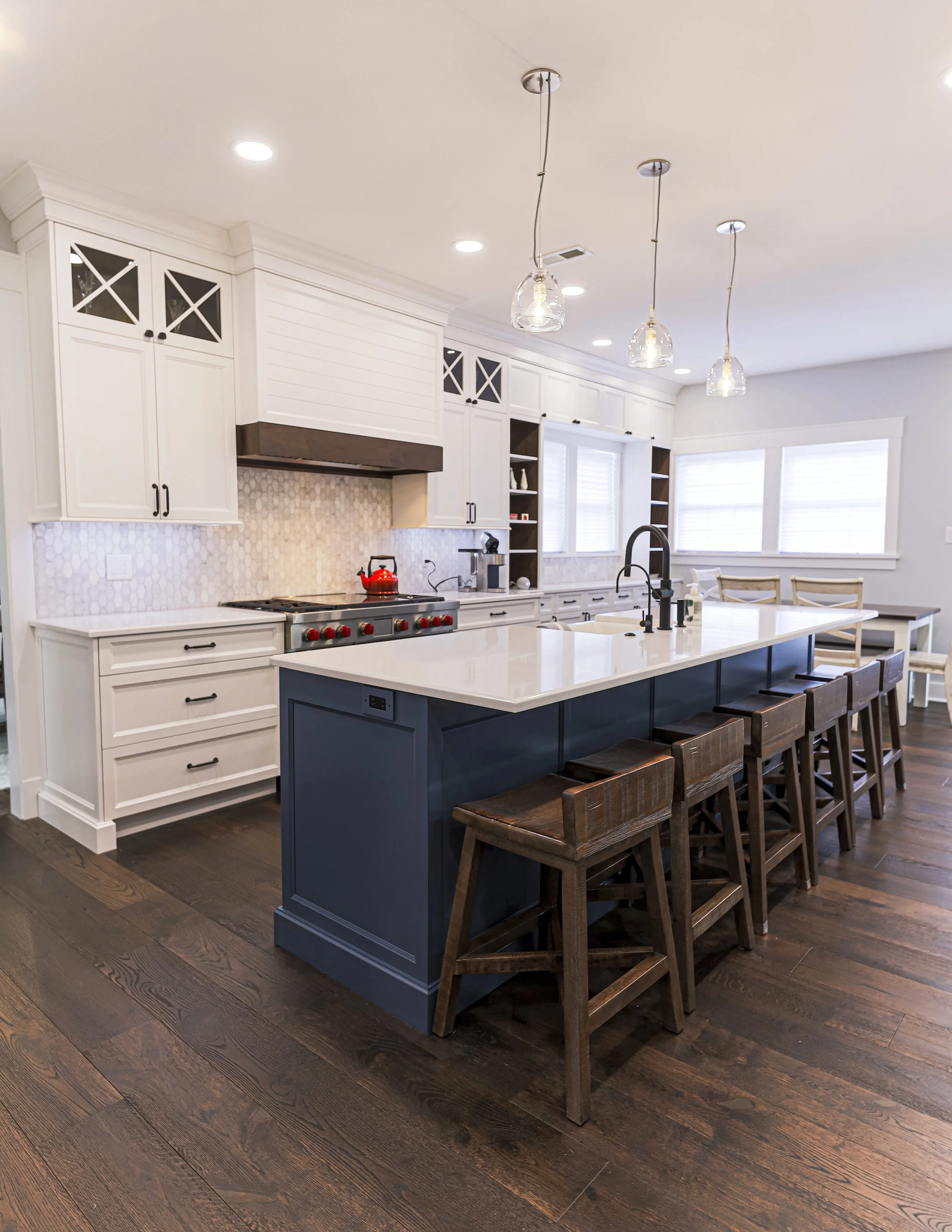 White kitchen with navy island, glass pendant lights and wood counter stools
