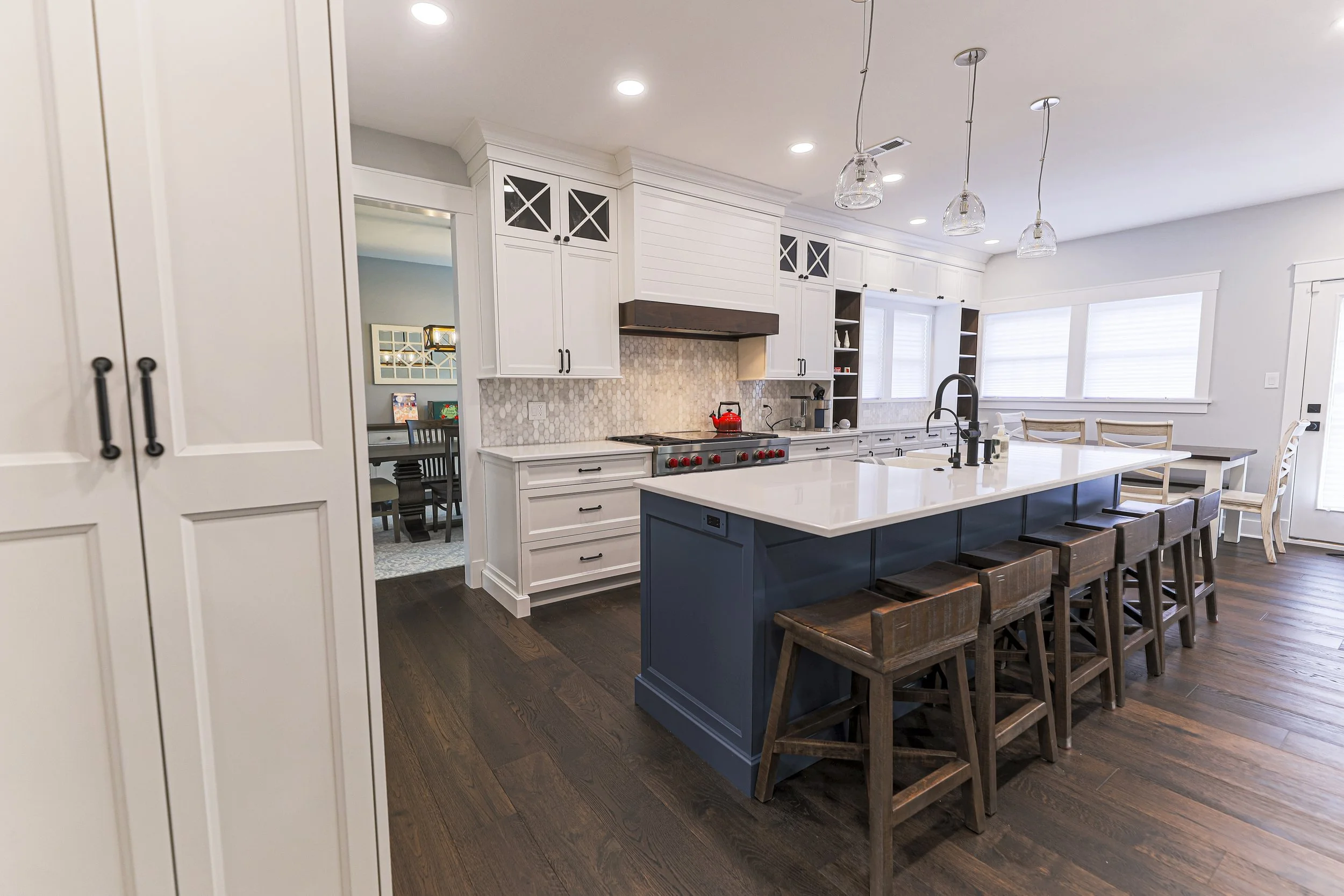 White kitchen and navy island seen past a tall pantry cabinet