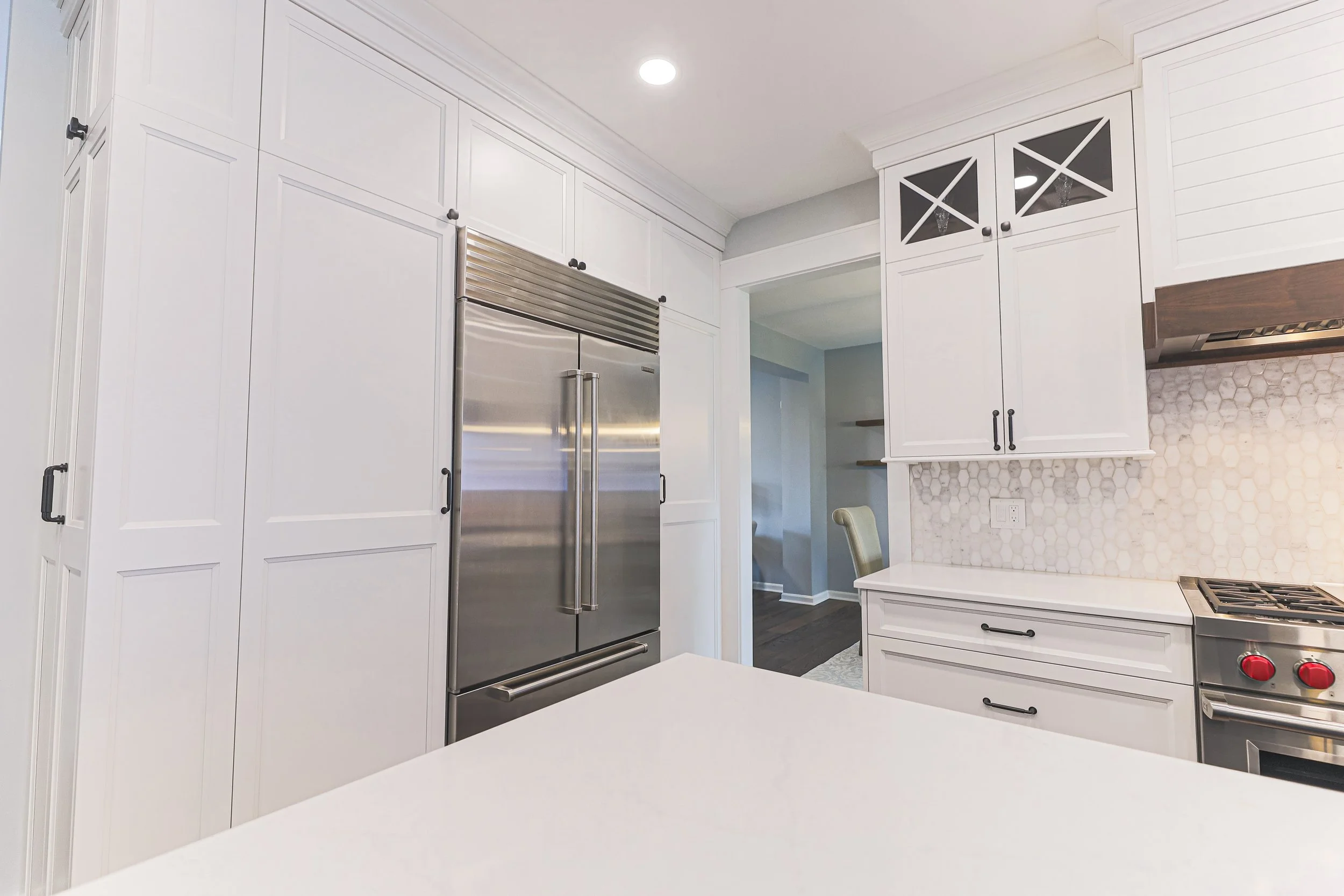 Built-in stainless refrigerator framed by white panel pantry cabinets