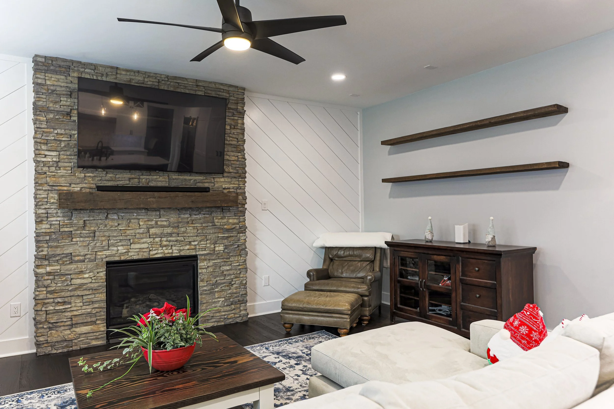 Family room with stacked-stone fireplace, rustic wood mantel and floating shelves
