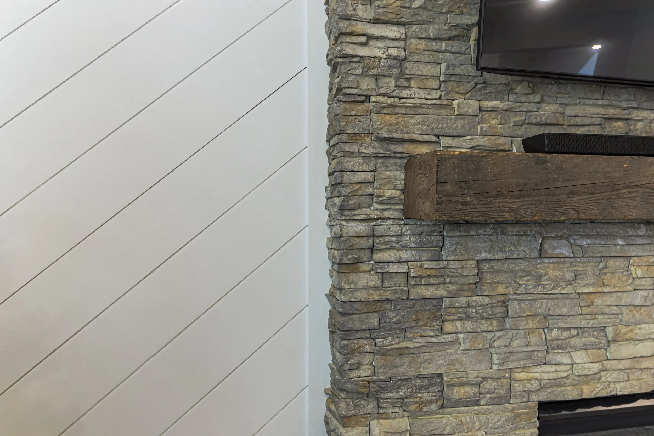 Stacked-stone fireplace and rustic mantel beside a diagonal shiplap wall
