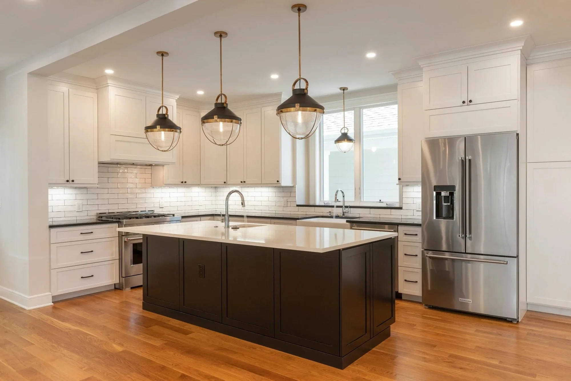 White shaker kitchen with a dark island, subway tile and lantern pendants