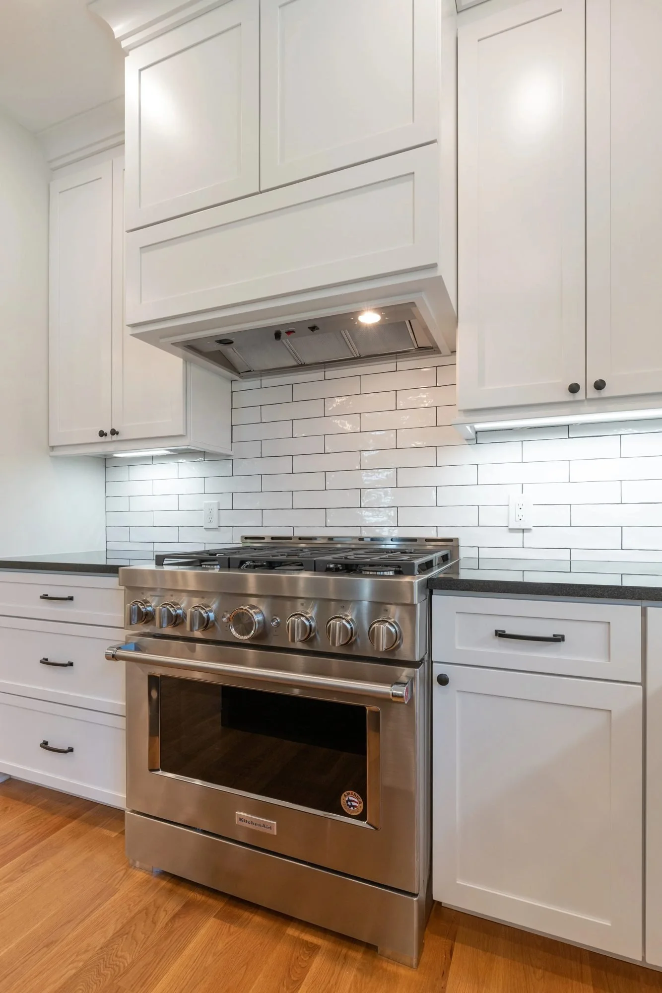 Stainless gas range under a white hood with subway tile backsplash