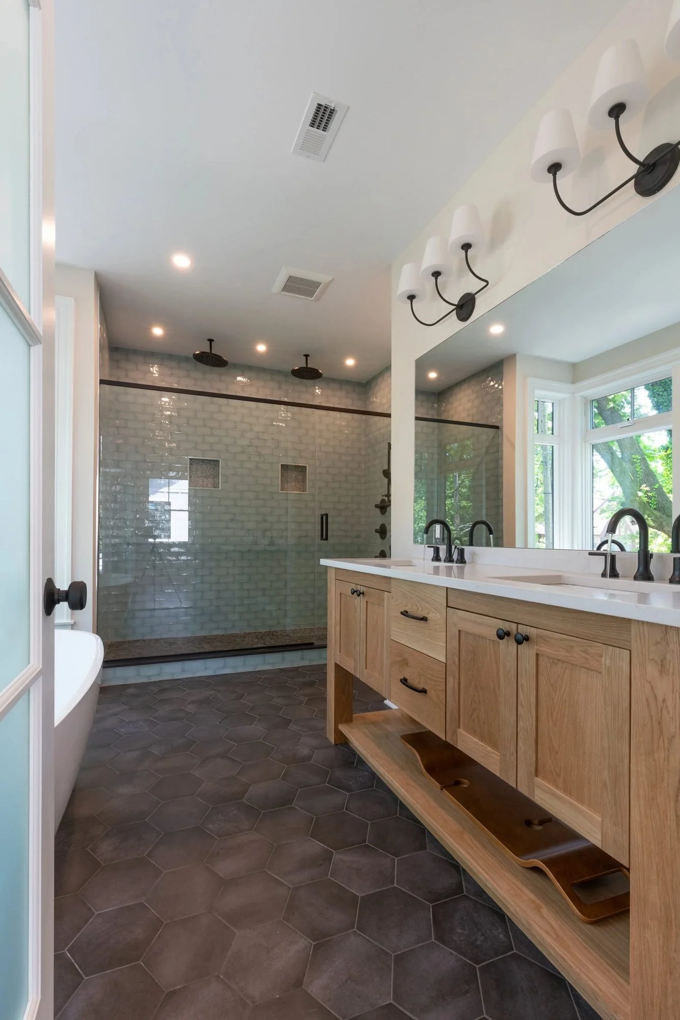 Primary bath with white oak double vanity and dark hexagon floor tile