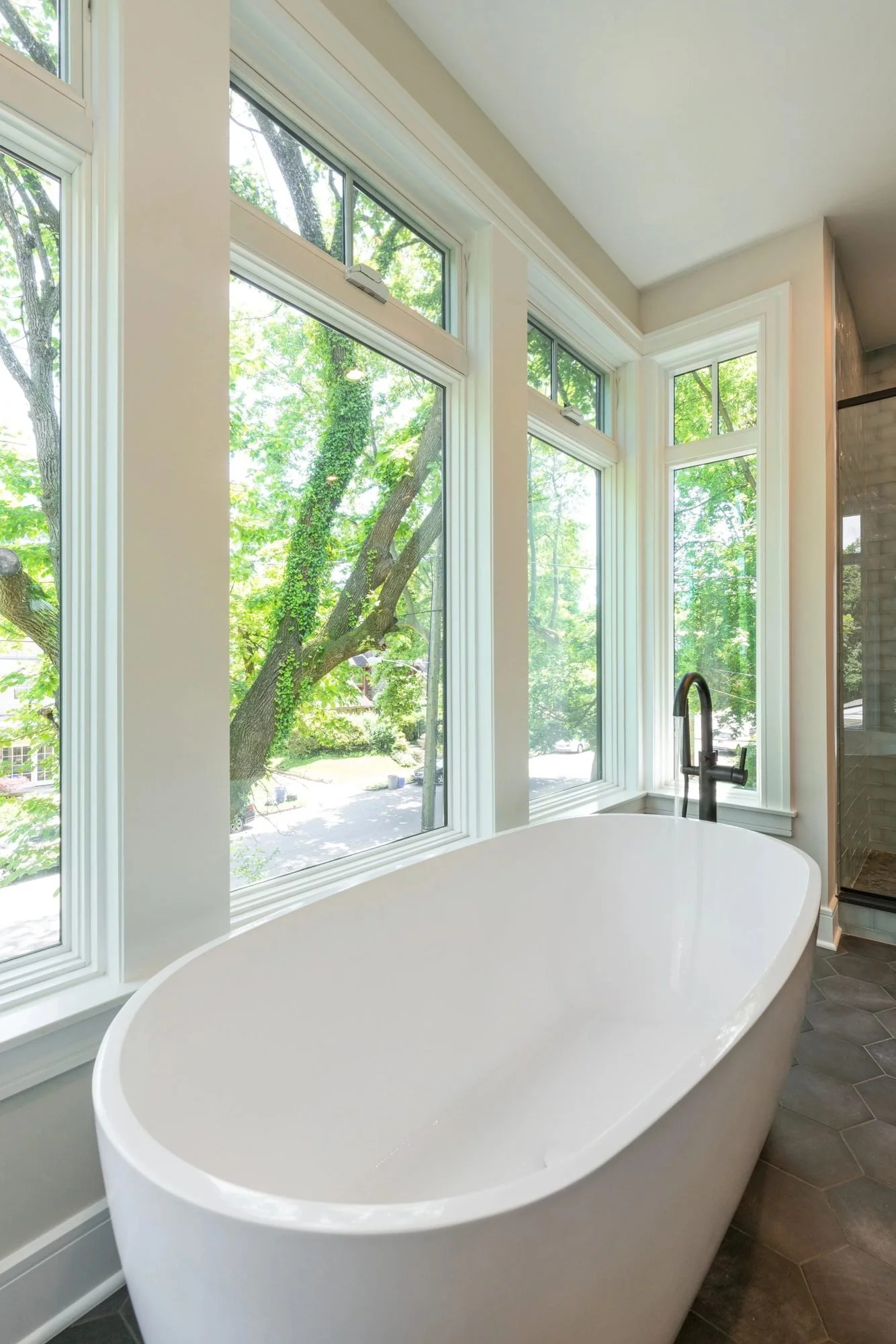 Freestanding soaking tub beneath corner windows with treetop views