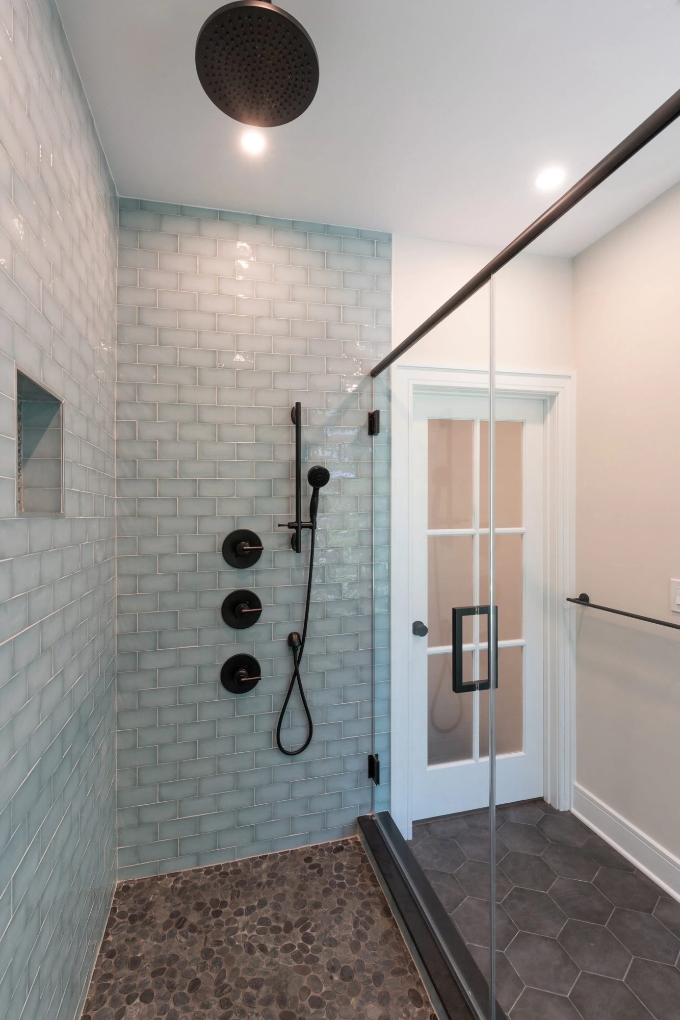 Glass subway tile shower with niche and black handheld sprayer