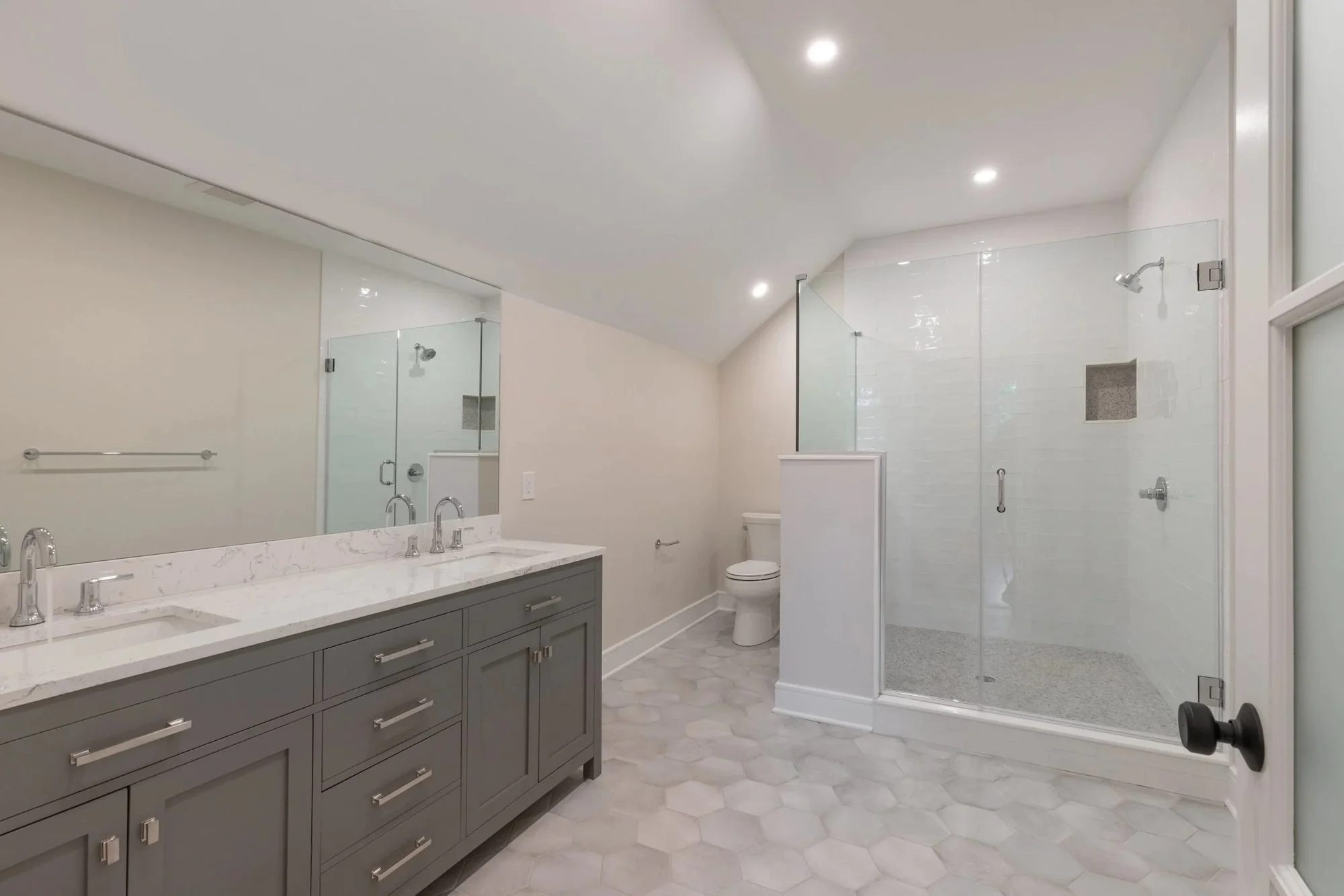 Bathroom with gray double vanity and glass shower under a vaulted ceiling
