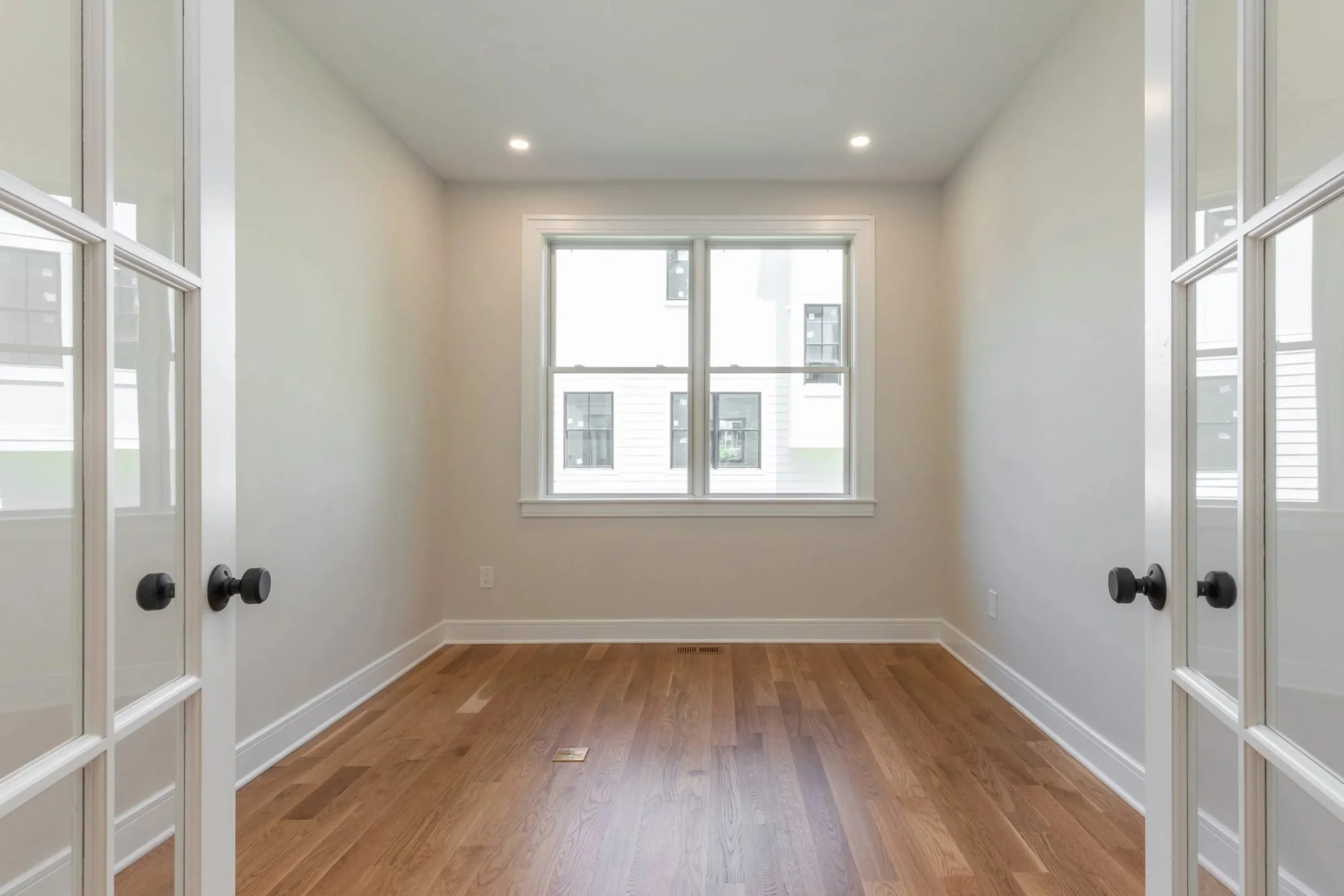 Room behind French doors with hardwood floors and a picture window