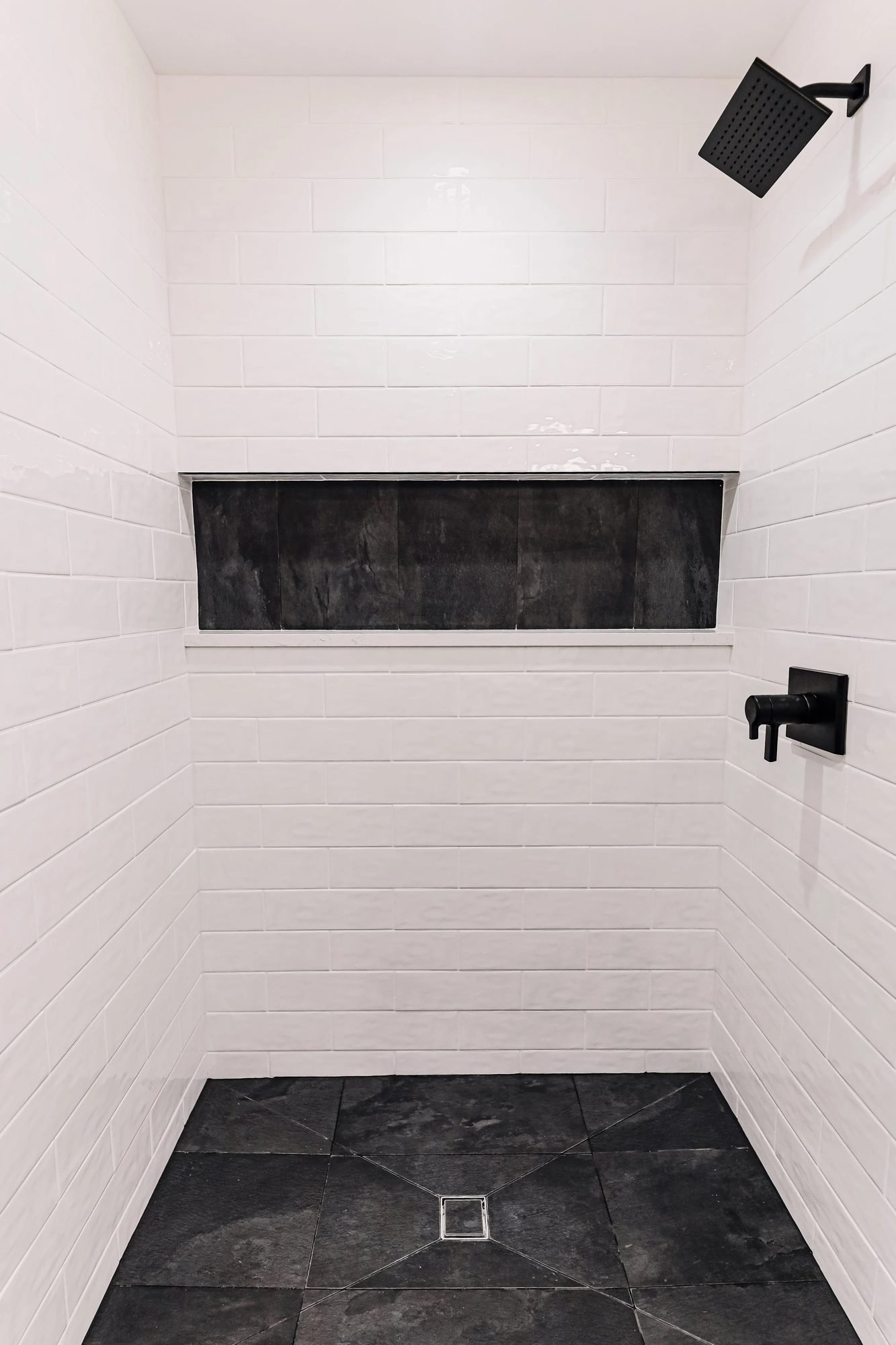 Walk-in shower with white tile walls, black slate floor and matte black fixtures
