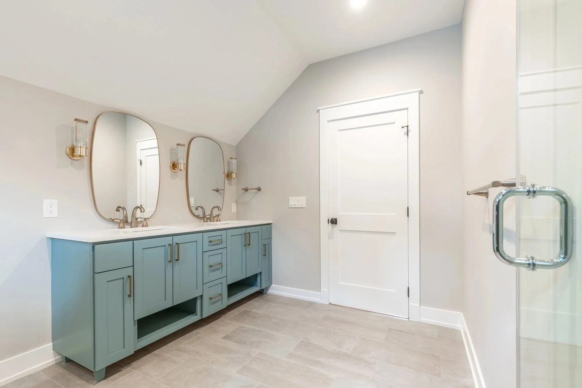 Teal double vanity with oval mirrors and brass sconces