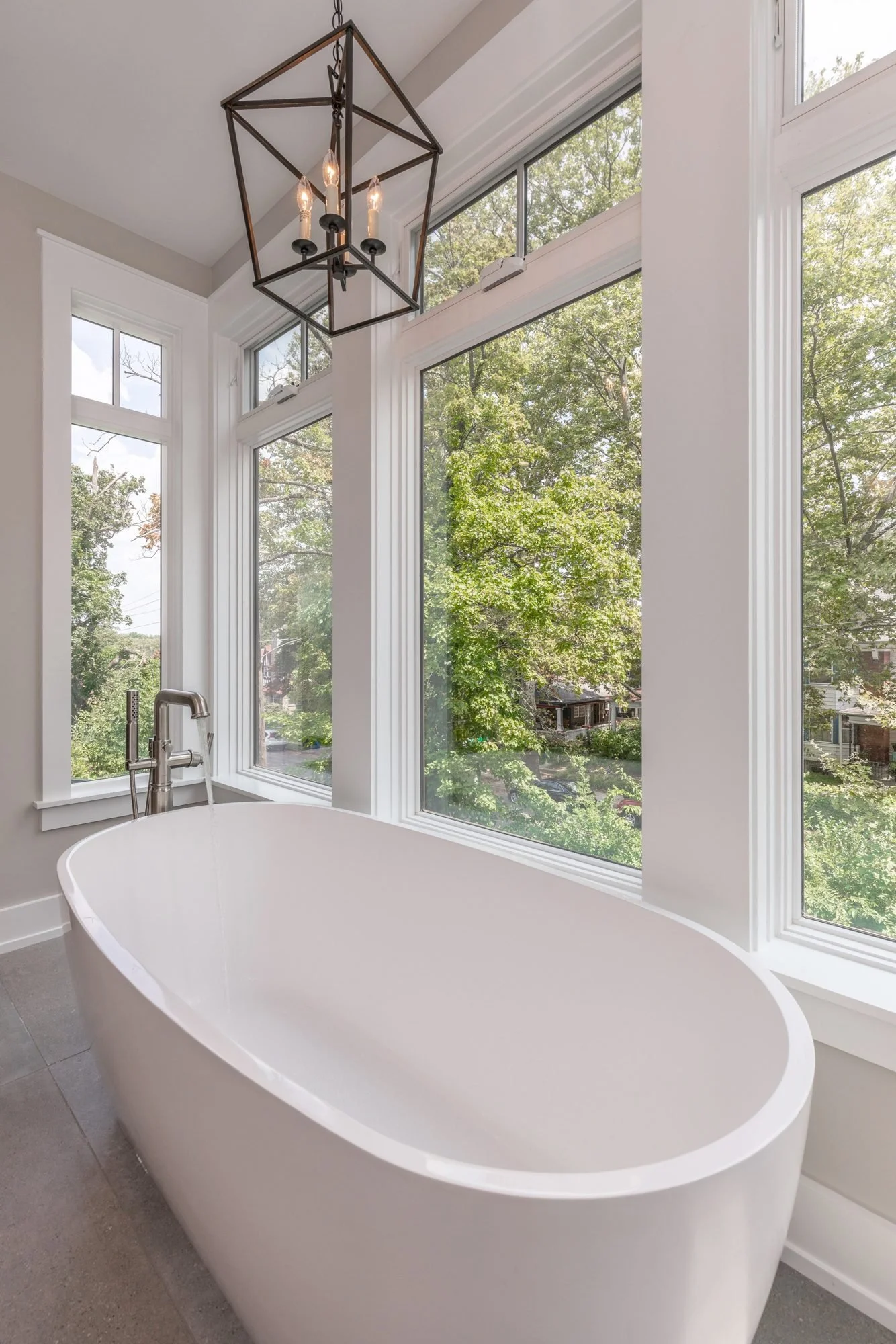 Freestanding tub under a lantern pendant by tall windows