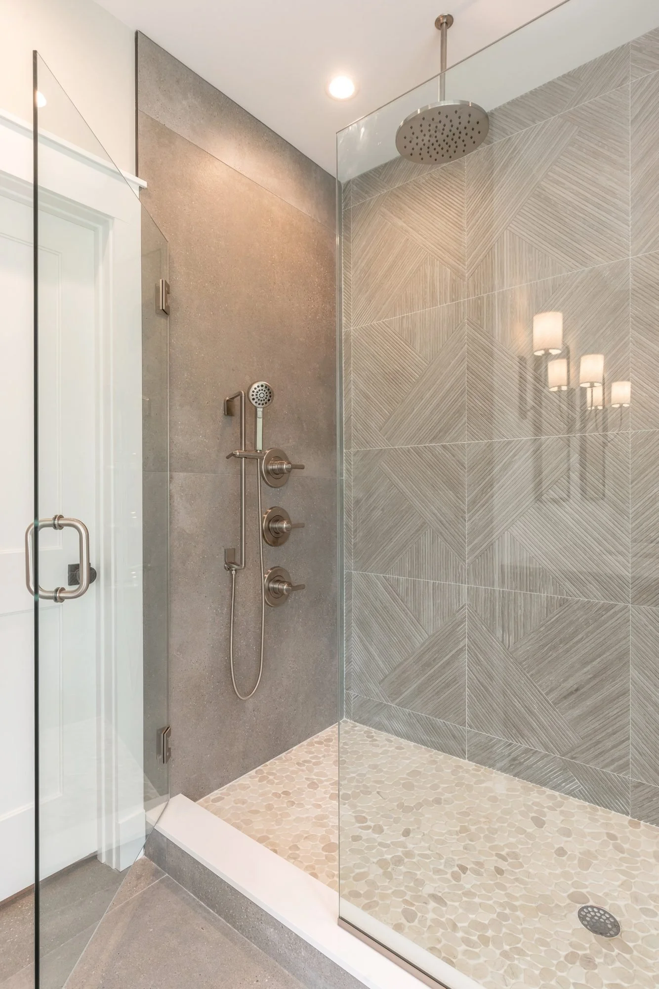 Gray tile walk-in shower with pebble floor and brass fixtures