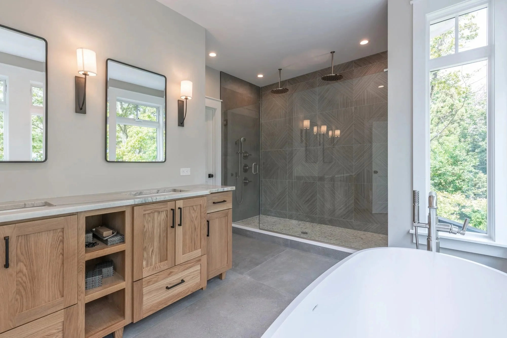 Primary bath with oak double vanity and gray tile walk-in shower