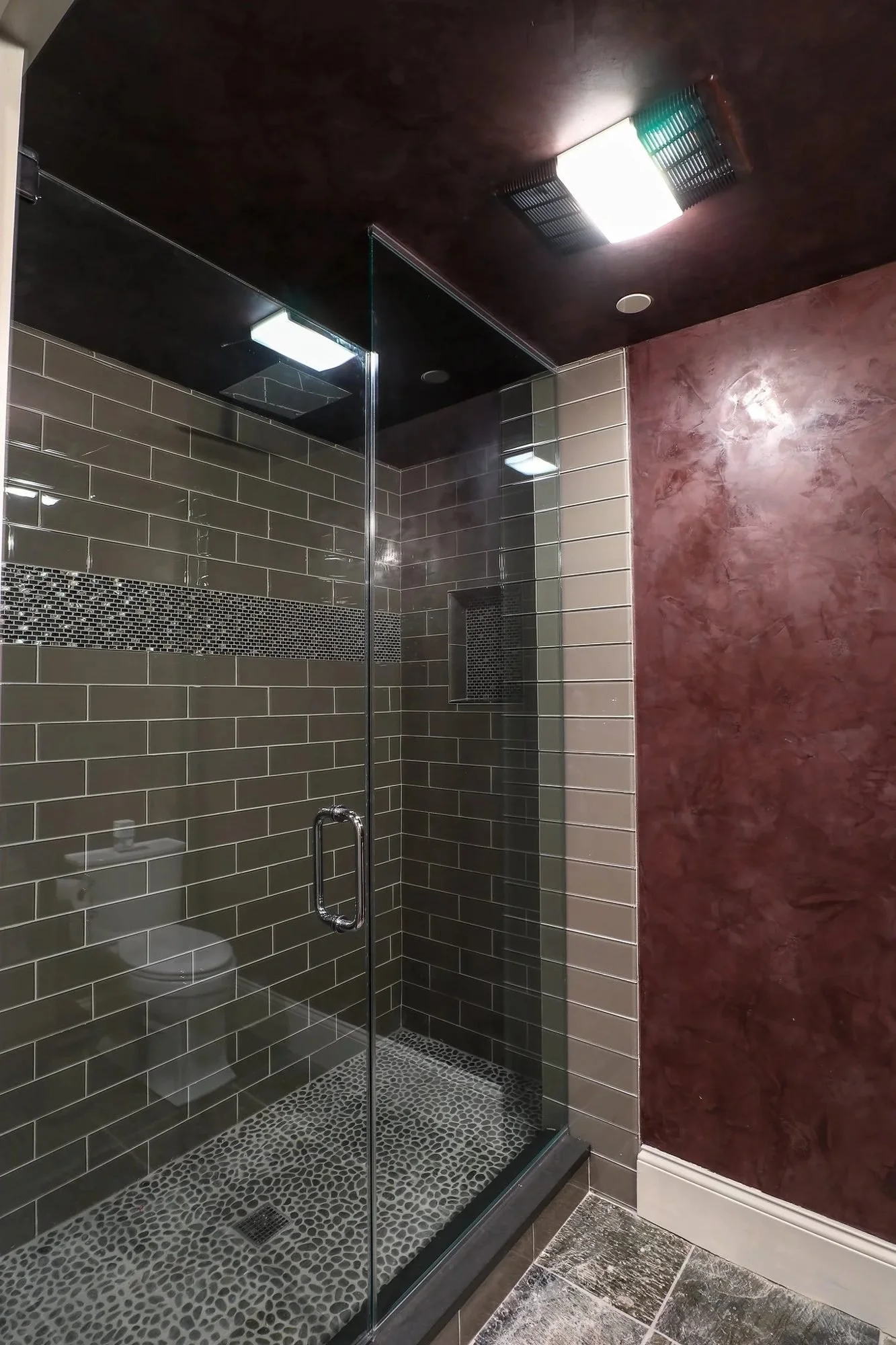 Glass shower with dark subway tile beside red Venetian plaster walls