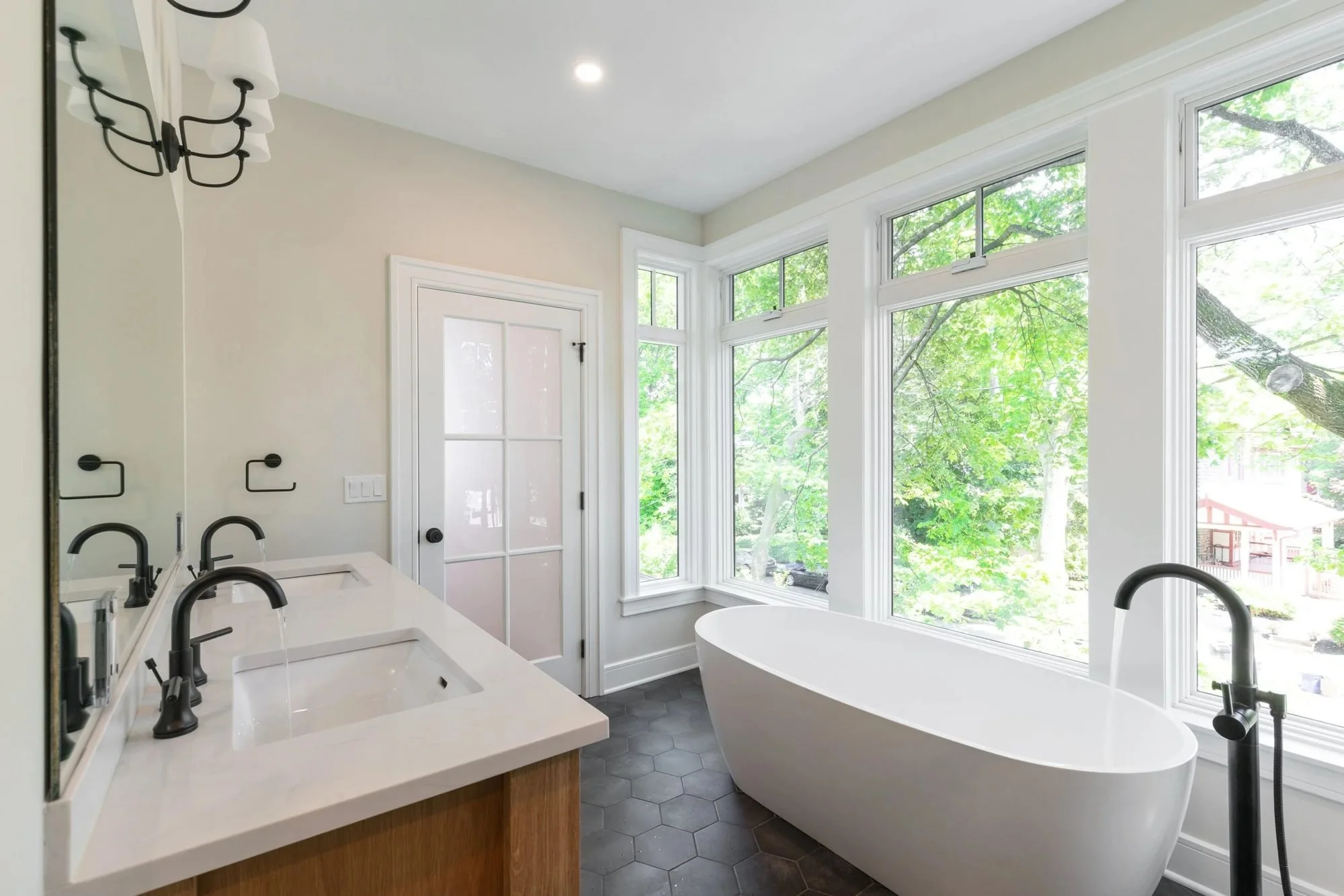 Primary bath vanity and freestanding tub by a wall of windows