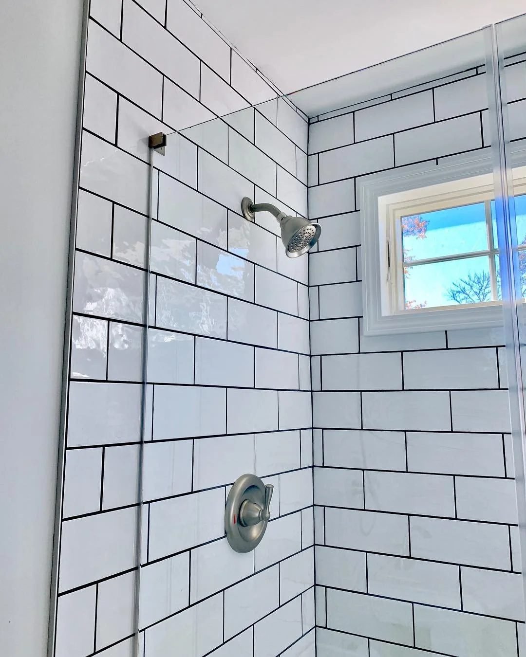 White subway tile shower with dark grout and a window